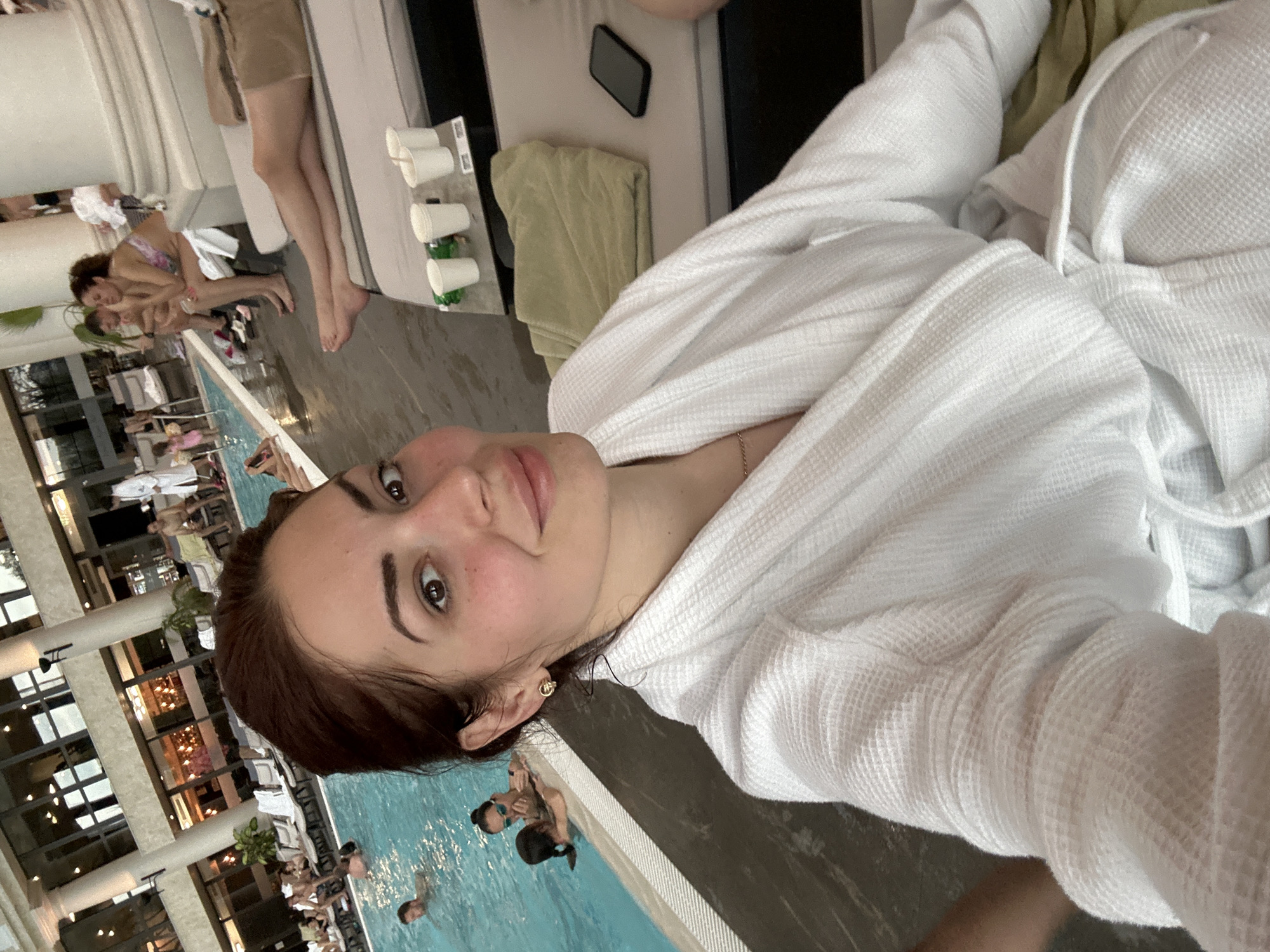 A woman in a white robe takes a selfie at the Aqua Park in Kazanlak, Bulgaria. A pool and other people are visible in the background.