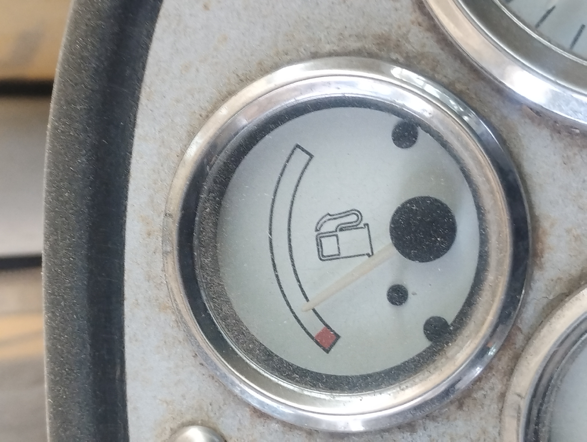 The image shows a close-up view of a dusty fuel gauge on a vehicle. The gauge has a needle pointing to the very left side, indicating a near-empty fuel tank. A red section on the left side of the gauge signifies the low fuel warning area. A stylized gas pump icon is visible on the face of the gauge. The surrounding area appears to be part of a vehicle's dashboard, with a dirty, textured surface and a thick rubber trim at the top. The location in the city of Sredets, Bulgaria, is not discernible from the image itself.
