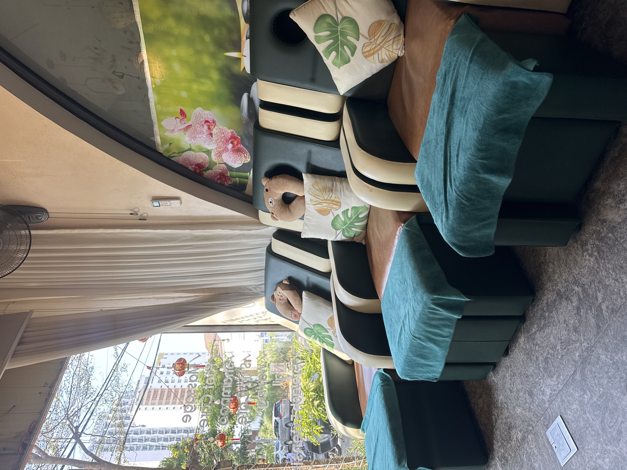 The interior of a foot care salon in Đà Nẵng, Vietnam is shown. Foot massage chairs with cushions are visible, as well as street scenes from outside the salon's window. Decorations in celebration of Lunar New Year are seen hanging outside.