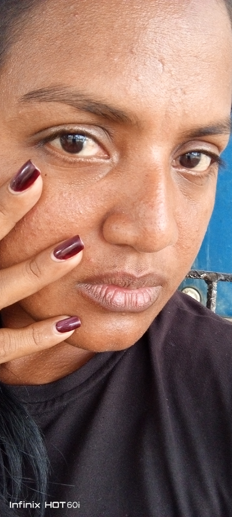 A close-up photograph depicts a dark-skinned person with reddish-brown painted nails on their fingers. The person's face fills the frame, with a dark-colored shirt visible below. There are no readily identifiable landmarks or contextual clues to specifically locate the subject in Altagracia, Venezuela, or any other city. The phrase "Infinix HOT 60i" is visible in the bottom left corner, implying the photograph was taken with that phone model.