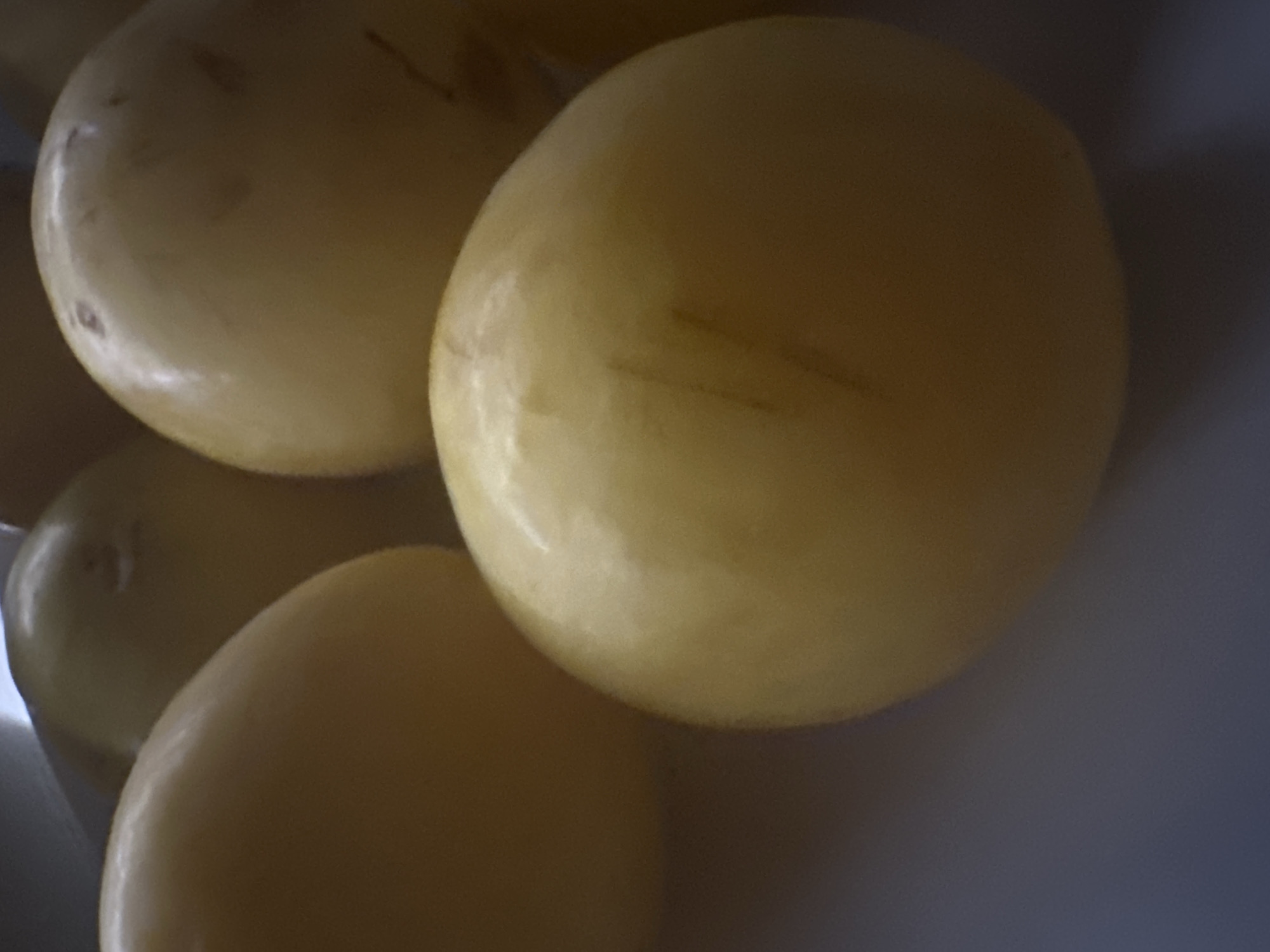 The image is a close-up shot of several yellow, oval-shaped fruits, possibly passion fruits or a similar variety. The fruits are densely packed and fill most of the frame. One fruit in the foreground has visible scratch marks on its surface. The lighting is soft, creating a warm glow on the fruits, and the background is blurred, suggesting a shallow depth of field. The image does not contain any elements that would indicate a specific location in Minsk, Belarus.