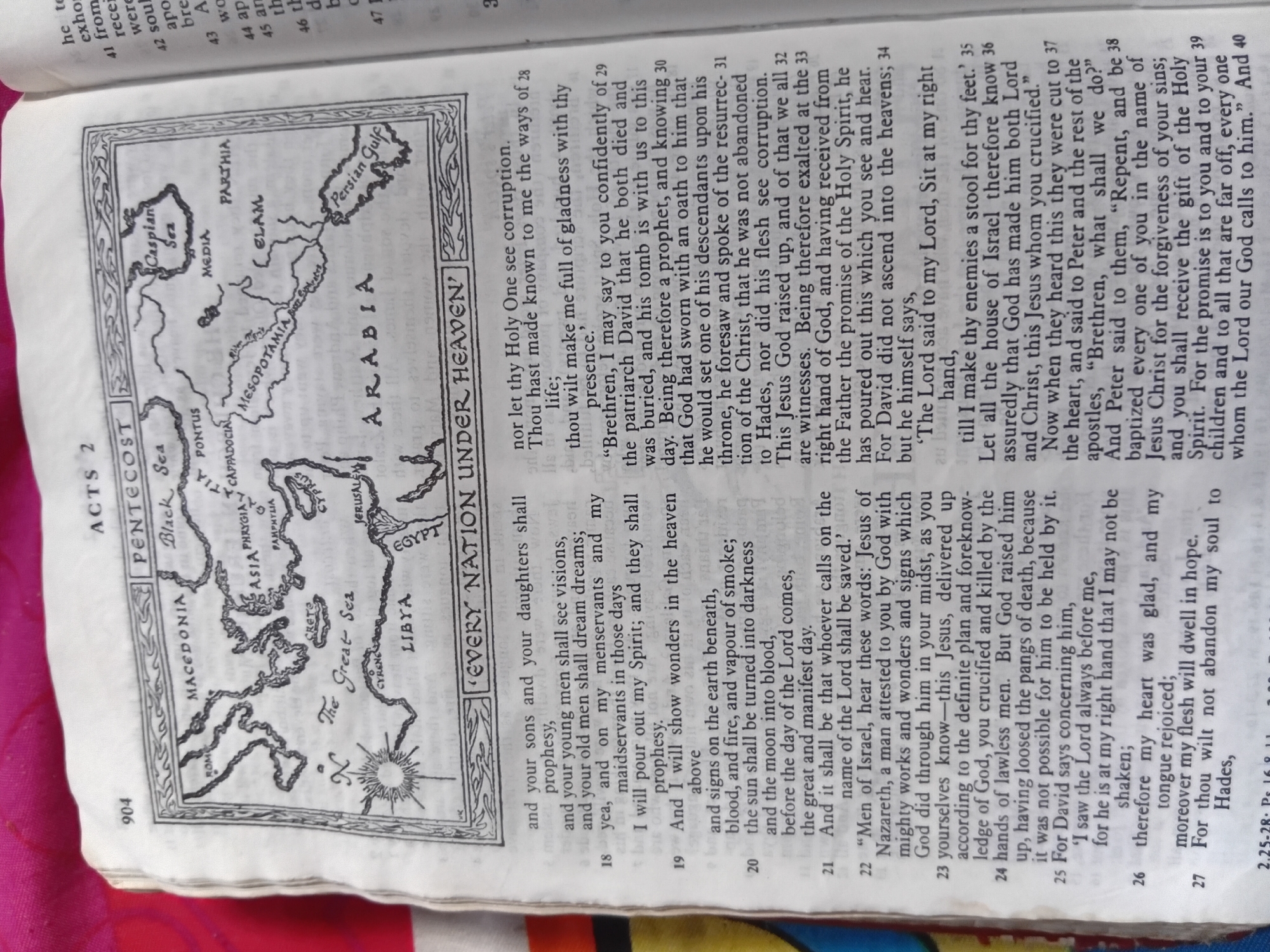 The image displays two open pages of a book, likely a Bible, given the presence of chapter and verse numbers and religious text. The left page features a black and white illustration of a map, depicting regions such as Macedonia, Asia Phrygia, Pontus, Cappadocia, Mesopotamia, Elam, Arabia, and Egypt. The map is surrounded by a decorative border and includes labels for seas like the Black Sea, Caspian Sea, and the Great Sea, as well as the Persian Gulf. The text on both pages is in English.
The right page contains numbered verses of scripture, spanning from verse 28 to verse 40. The text discusses biblical events and teachings, including prophecies, the outpouring of the Holy Spirit, the resurrection of Jesus, and calls to repentance and baptism. Specific phrases like "Every Nation Under Heaven," "nor let thy Holy One see corruption," and "the promise of the Holy Spirit" are visible. The page numbers "904" and "3" are also present. The overall impression is that of a religious text providing historical and theological context, possibly related to the early Christian church given the mention of Pentecost and apostles. The material appears to be printed paper, with the binding of the book partially visible on the left side.