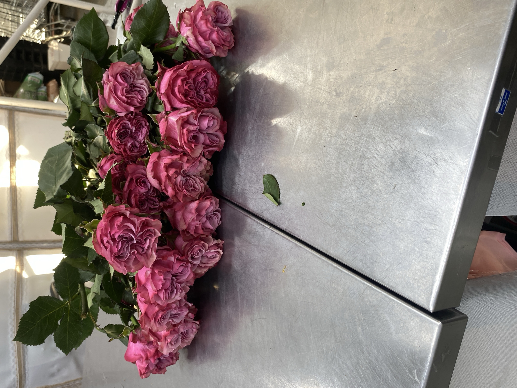 A cluster of pink roses with green leaves is arranged on a stainless steel surface. The steel surface appears to be two adjoining sections, possibly part of a worktable or counter. The environment suggests an indoor setting, possibly a florist's shop or a workshop. The image location cannot be determined from the visual information, and there is no confirmation of it being in Yekaterinburg, Russia.