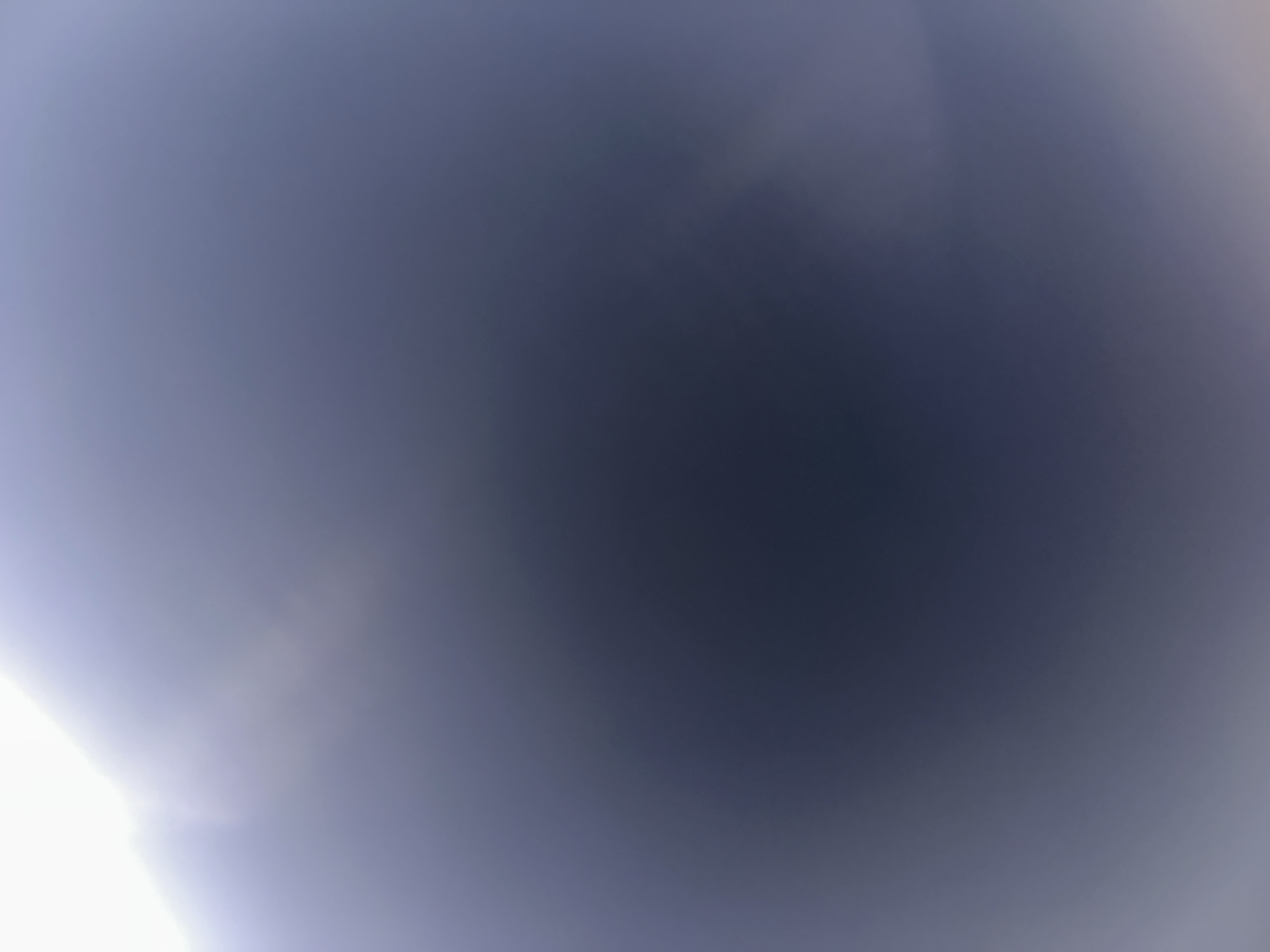 The image is an abstract, out-of-focus photograph dominated by shades of dark blue and gray, with a bright, blown-out white area in the upper right corner. There are no discernible subjects, objects, people, or actions. The texture is soft and gradient-like, suggesting a diffuse light source or lens flare. It is not possible to determine the location in Belgrade, Serbia, or any specific scene details from this image.