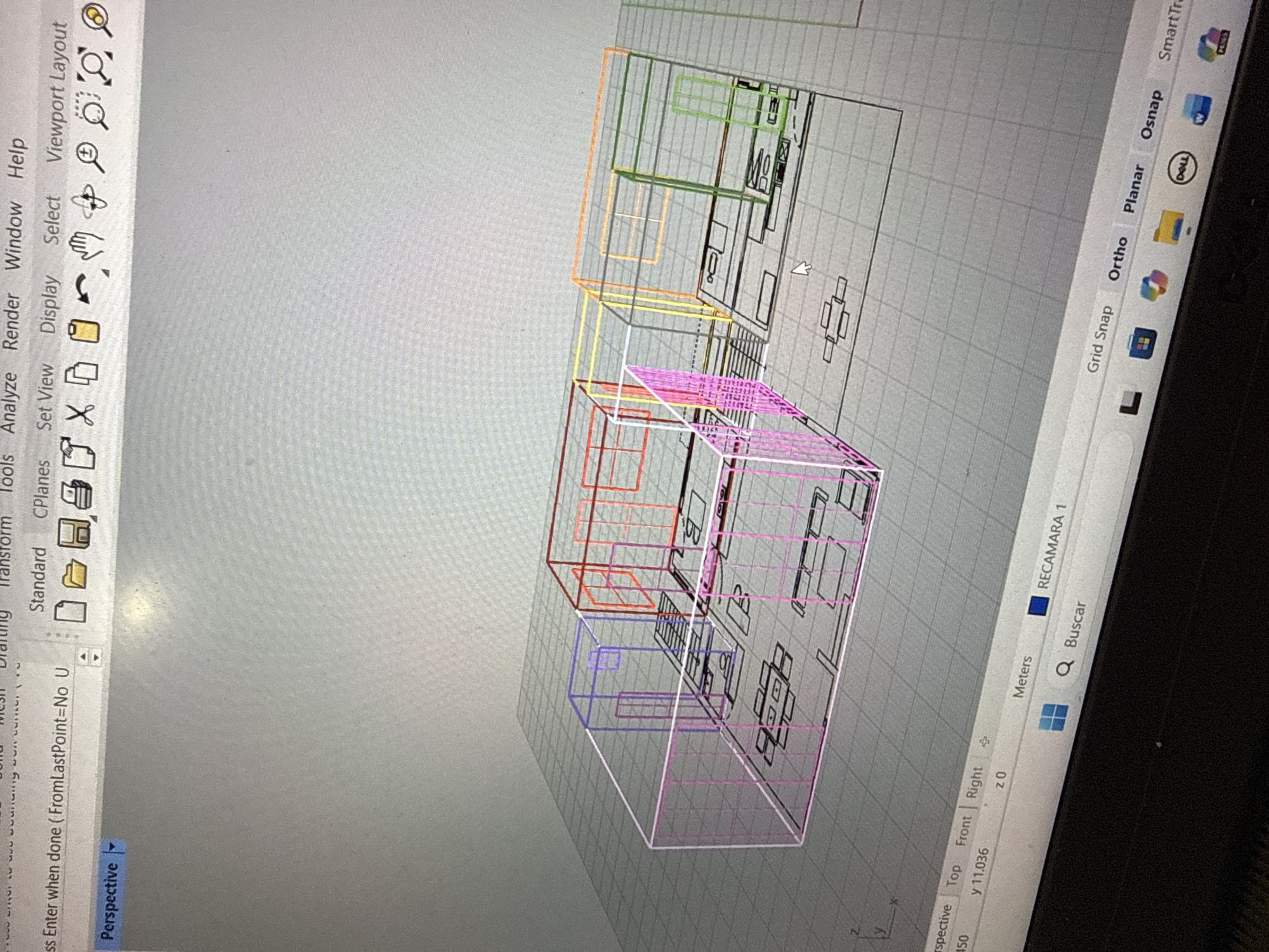The image shows a computer screen displaying a 3D model in a CAD software, likely Rhino. The model appears to be an architectural design, possibly of a multi-story building or a house. The design is represented using wireframe lines, with different sections highlighted in colors like orange, green, yellow, red, pink, and blue. The environment consists of the CAD software user interface, including menus such as "Tools," "Analyze," "Render," "Window," and "Help." The view is set to "Perspective." Additional interface elements, such as "Grid Snap," "Ortho," "Planar," and "Osnap," are also visible. The text "RECAMARA 1" is displayed on the screen. There's no information in the image to suggest that this is in Puebla, Mexico.