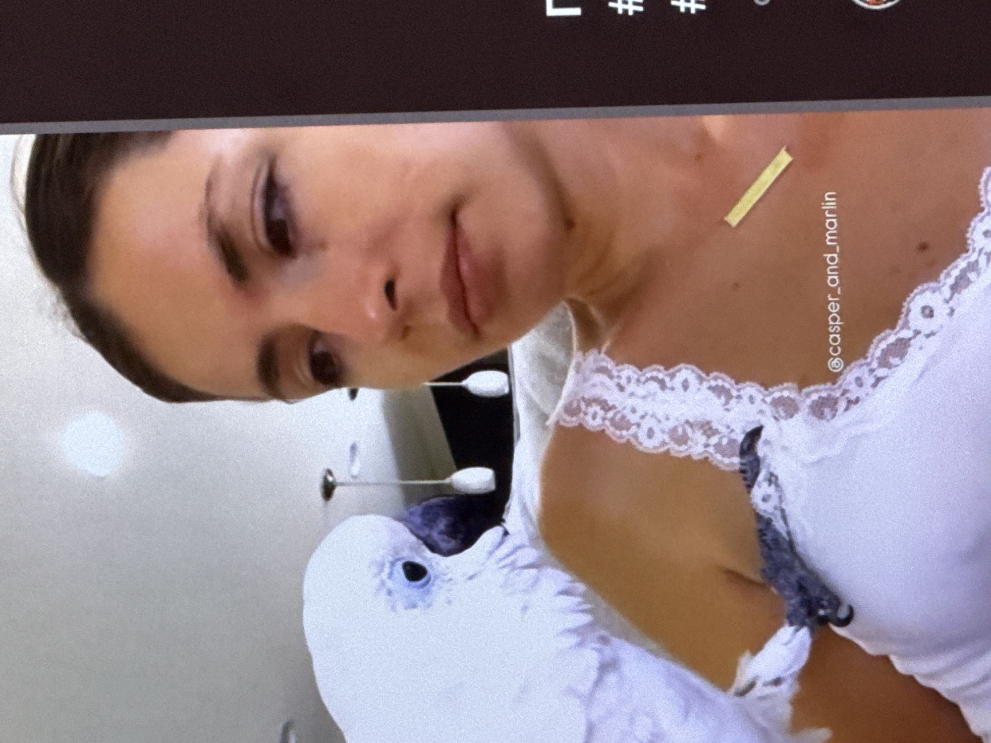 A close-up shot shows a woman and a white cockatoo. The woman is looking to the right, with her face partially visible. She is wearing a white top with lace trim. The cockatoo is perched on her shoulder and is facing left, with its eye visible. The background is out of focus and appears to be an indoor setting with lights. There is text overlaid on the image, including "@casper_and_marlin". The scene is not located in the city of Cahul, Moldova.