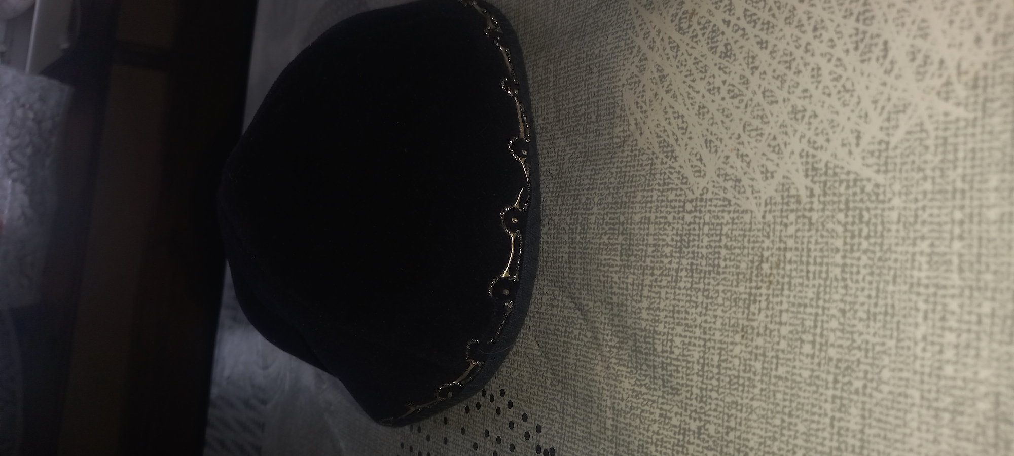 A black hat with gold trim lies on a patterned surface. The scene also includes a dark brown and white area. The location in Kryvyi Rih, Ukraine is not discernible.