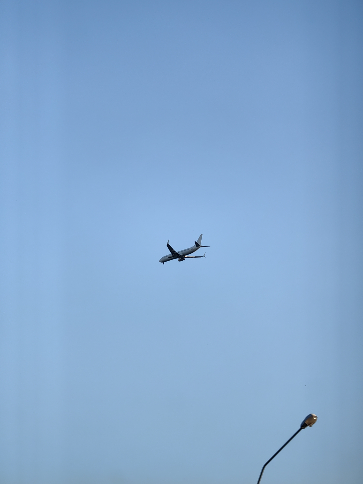 An airplane is visible in the bright blue sky. Below the airplane, a streetlamp is partially visible in the bottom right corner of the image. The scene is likely in Забалоцкі сельскі Савет, Belarus.