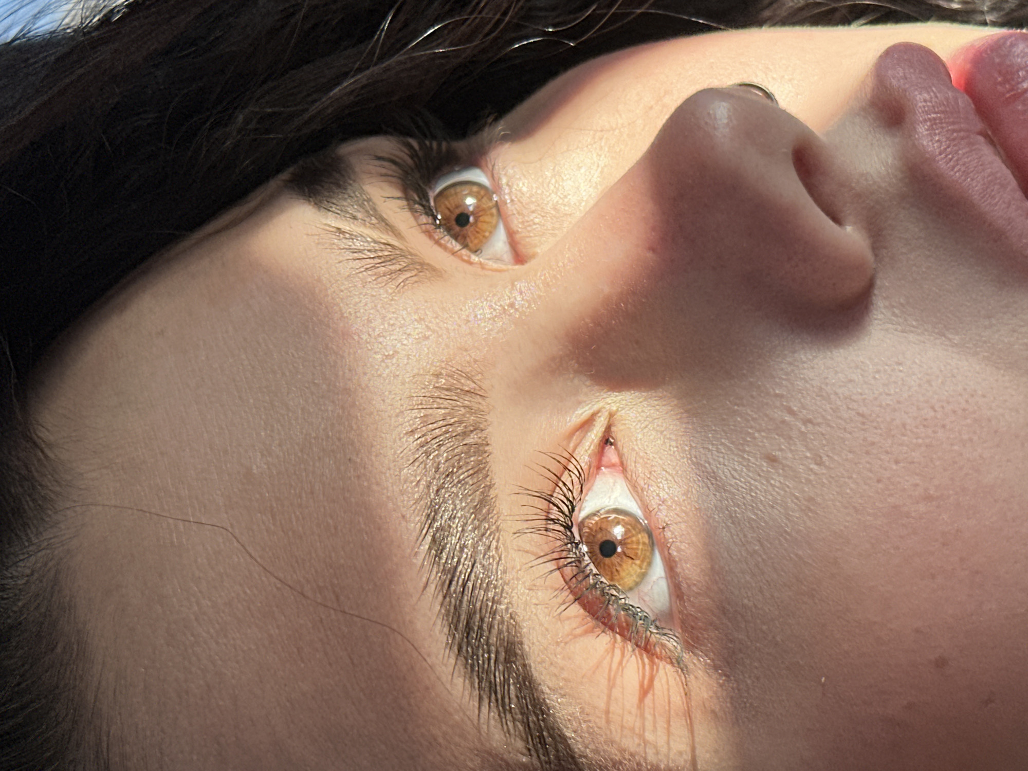 The image is a close-up, upward-angled shot of a person's face. The focus is primarily on the eyes, nose, and lips. The eyes are hazel in color, with visible eyelashes and eyebrows. The skin tone is fair. A shadow partially covers the face. The person's hair is dark. The background is out of focus. There is no information to indicate this was taken in Kazan, Russia.