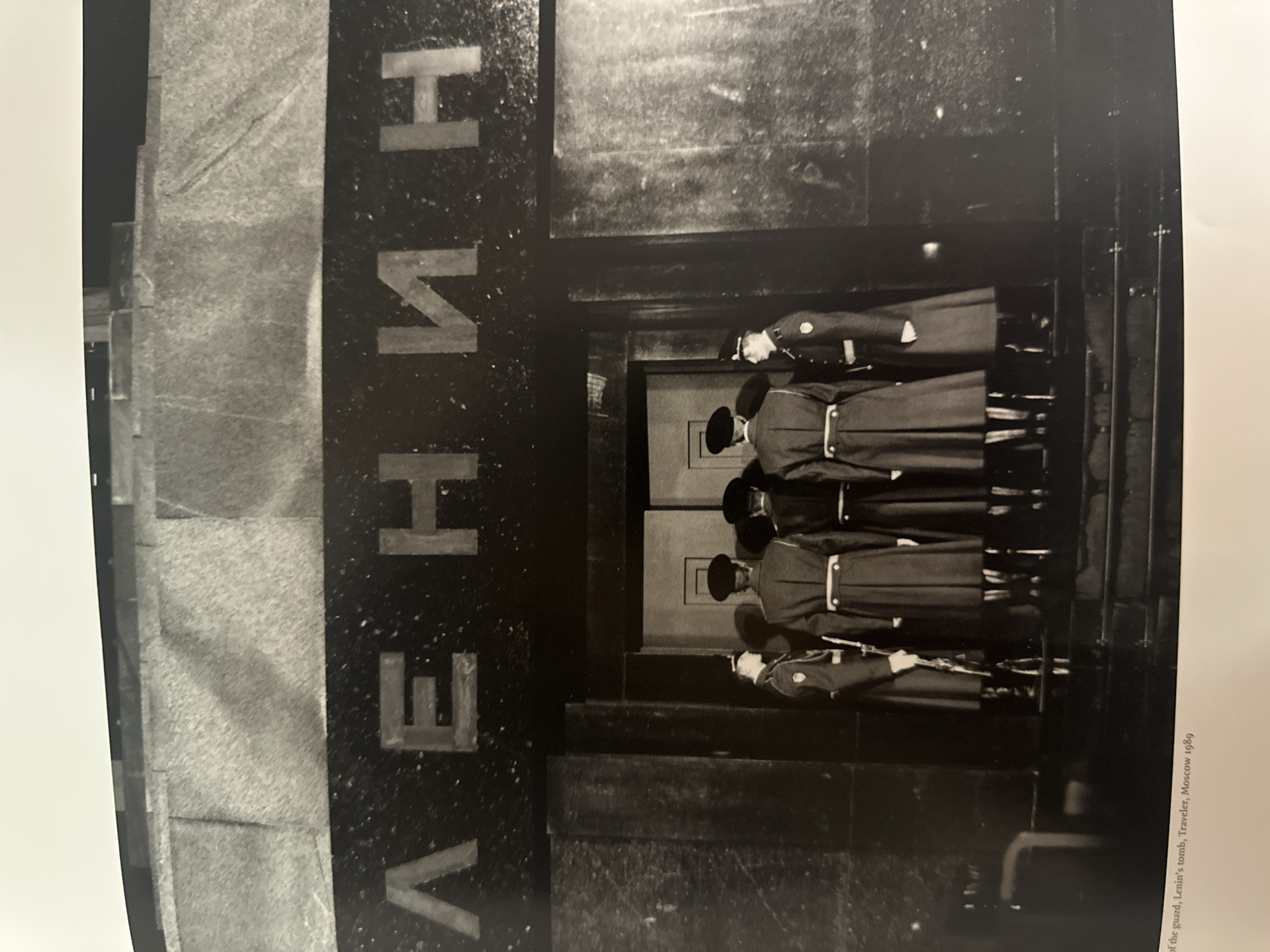 The black and white photograph shows soldiers standing guard at Lenin's Tomb in Moscow, Russia in 1989. The tomb's exterior is marked with the Russian word "ВЕЧНЫЙ" (Eternal). Six soldiers stand in two rows. The soldiers wear dark uniforms with light belts and carry rifles.