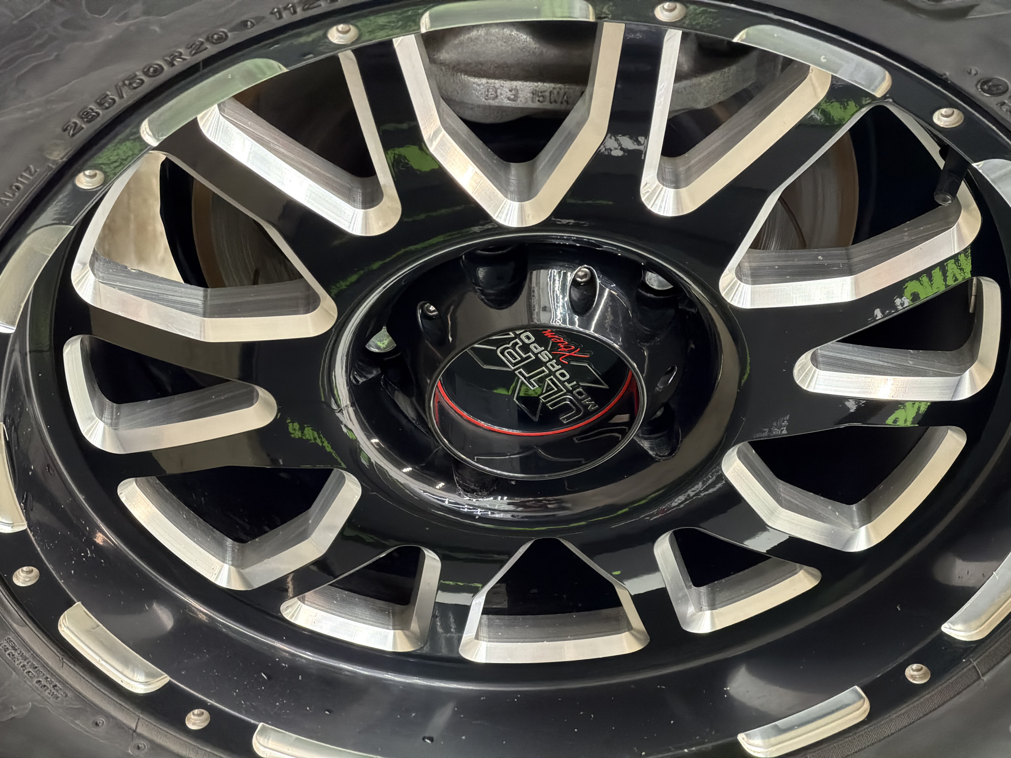 The image shows a close-up of a black and silver Ultra Motorsports wheel on a tire labeled "285/50R20 112". The wheel has a triangular spoke design with a black center cap featuring the Ultra Motorsports logo. The background is blurry, suggesting a vehicle setting. No specific location in Krasnoyarsk, Russia, is discernible from the image.
