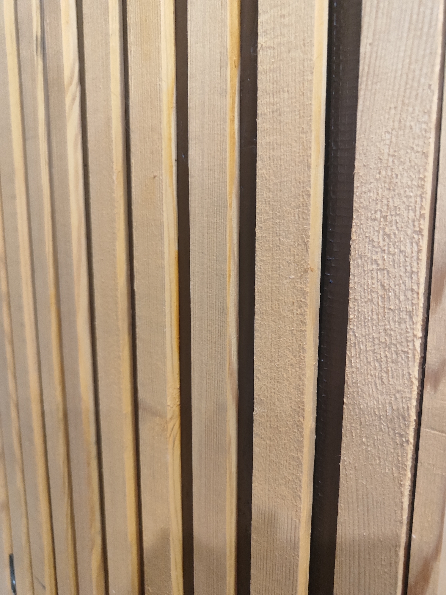 The image is a close-up, eye-level shot of a series of vertical wooden planks. The planks are light brown and appear to be unfinished, with visible wood grain and some rough texture on their surfaces. They are arranged closely together, with narrow dark gaps between them. The lighting is even, and the focus is sharp on the texture of the wood. The scene depicts an interior or outdoor surface constructed from these planks. There are no people or specific identifiable landmarks visible. The location in Salavat, Russia, cannot be determined from the visual information in the image.