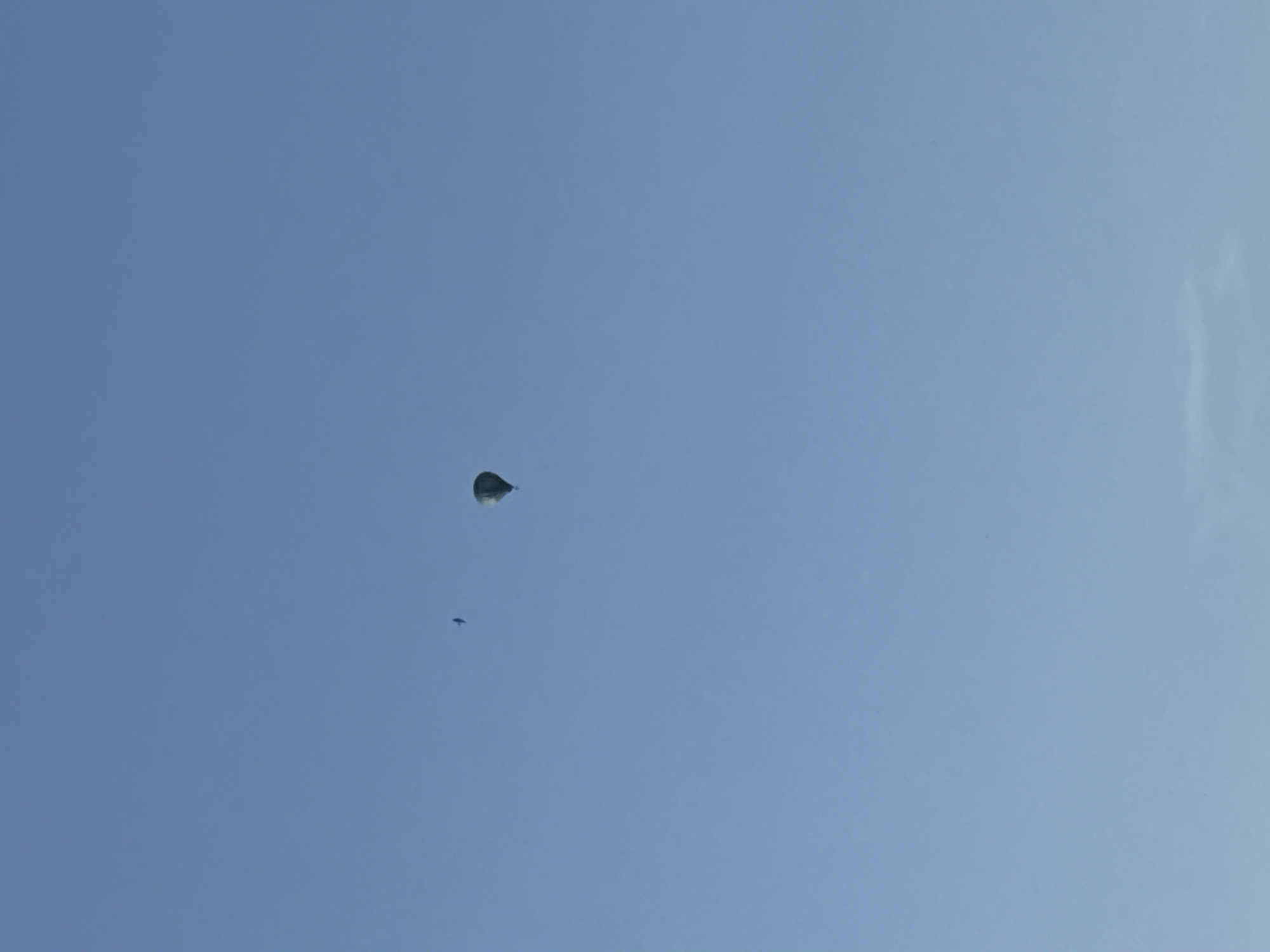 A hot air balloon is visible in the sky, along with a smaller, dark object that could be a bird or another aircraft. The sky is a clear, light blue.