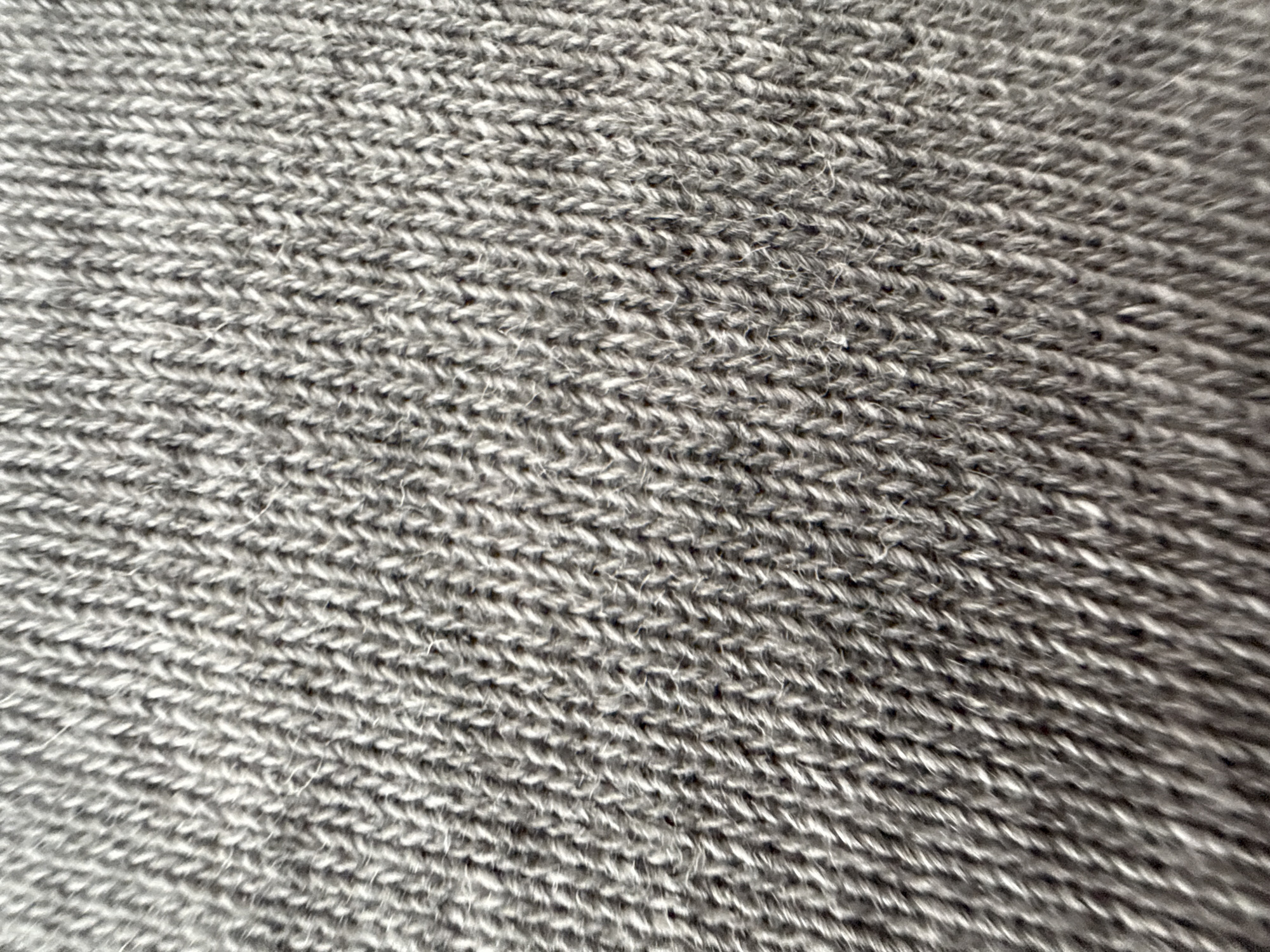 The image shows a close-up of gray knitted fabric. The individual stitches are clearly visible, forming a textured pattern of horizontal rows.