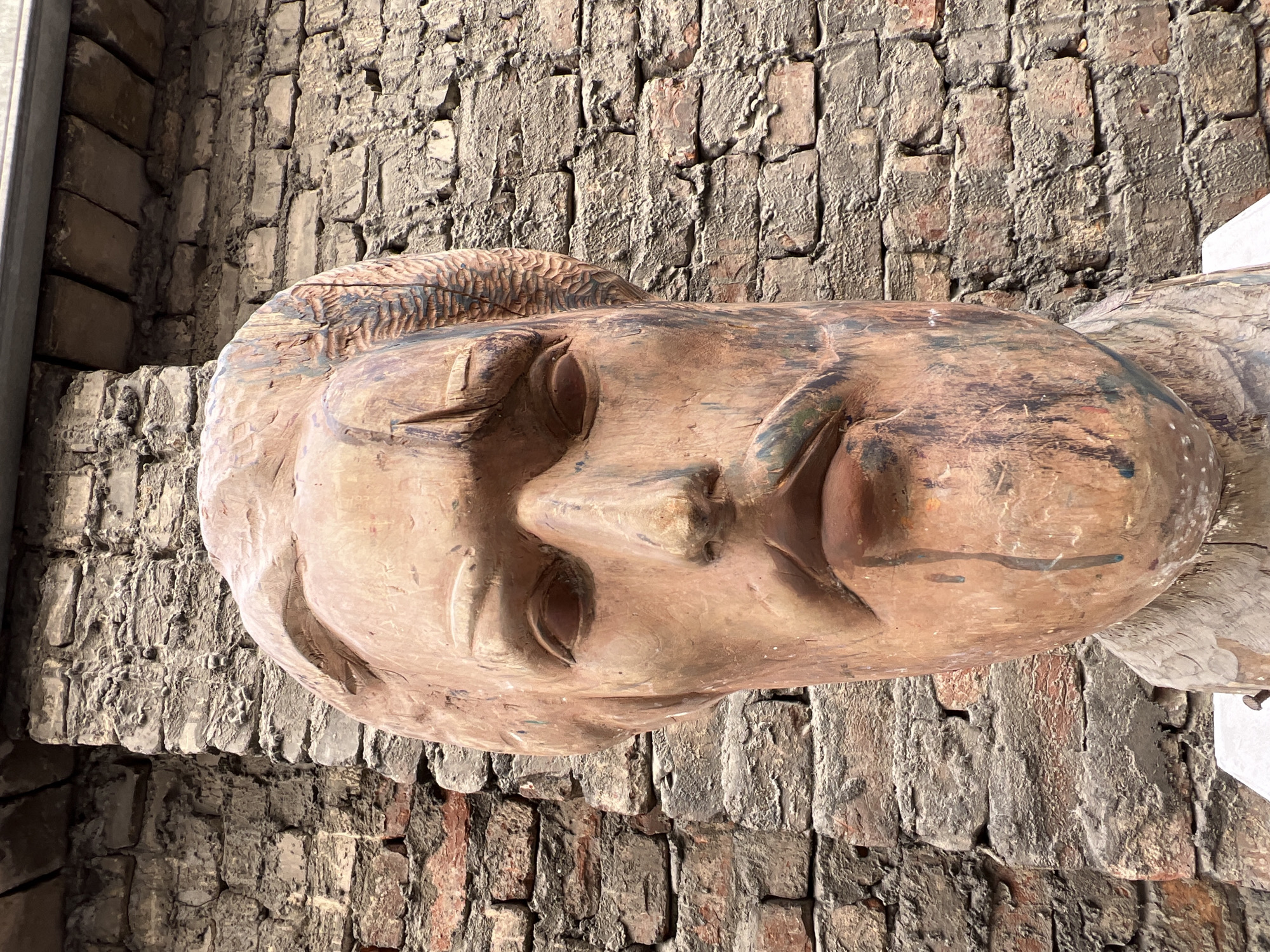 The image depicts a wooden sculpture of a face, possibly a mask or a decorative element, with a weathered appearance. The face features closed eyes and stylized features. The sculpture is placed against a weathered brick wall, suggesting an outdoor or semi-outdoor setting.
Although a precise location cannot be determined from this single image, considering the style of the sculpture and the brickwork, it is possible that this image was taken in St. Petersburg, Russia, but without any additional information or context, this can only be a hypothesis.
