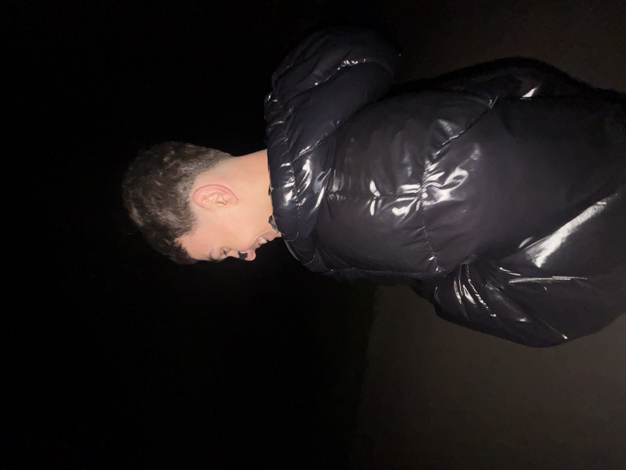 A person in a dark, shiny puffer jacket is illuminated against an otherwise dark background. The person is facing to the left and downwards, with their mouth open. They appear to have short, dark hair. The environment is poorly lit, making it difficult to discern specific details. No information suggests the location is in Lehchevo, Bulgaria.