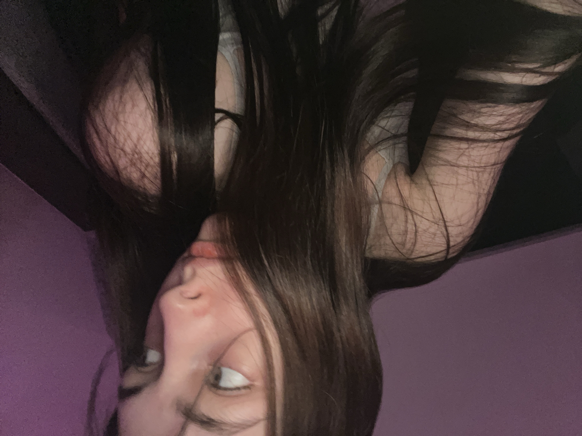 A photograph shows a woman's face upside down. She has dark hair. Her eyes are open and looking to the side. The background is a light purple wall. There is black fabric above her. The location in the city of Saint Petersburg, Russia, cannot be determined from the image.