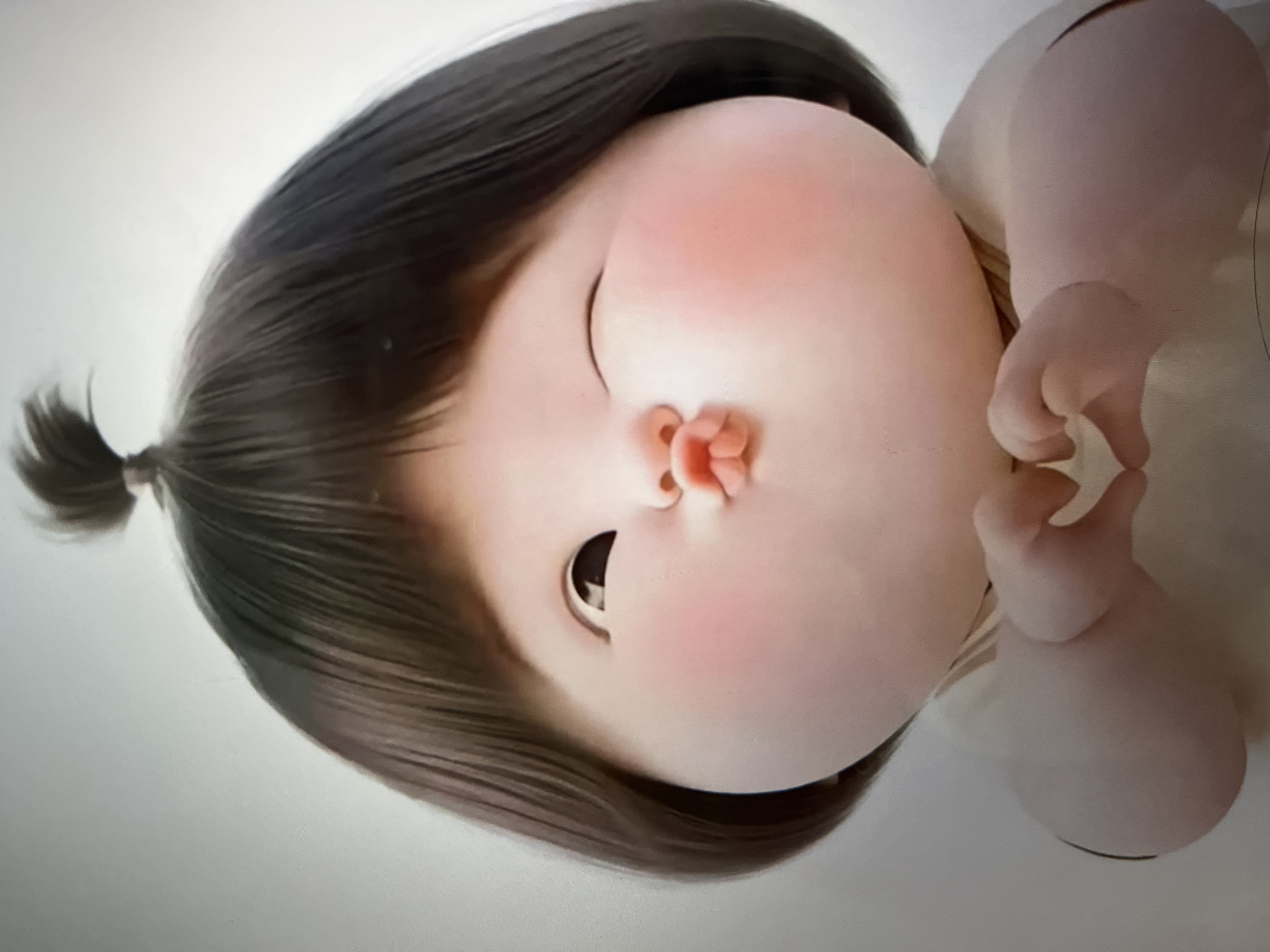 A 3D animated character of a young child is shown in a close-up, head and shoulders shot. The child has large, round cheeks, a small nose, and a puckered mouth, with one eye closed in a wink. The child's hair is dark brown and styled in a bob with a small ponytail on top. The child's hands are brought together in front of their chest, forming a heart shape. The background is a plain, light gray. The image appears to be a digital rendering.
