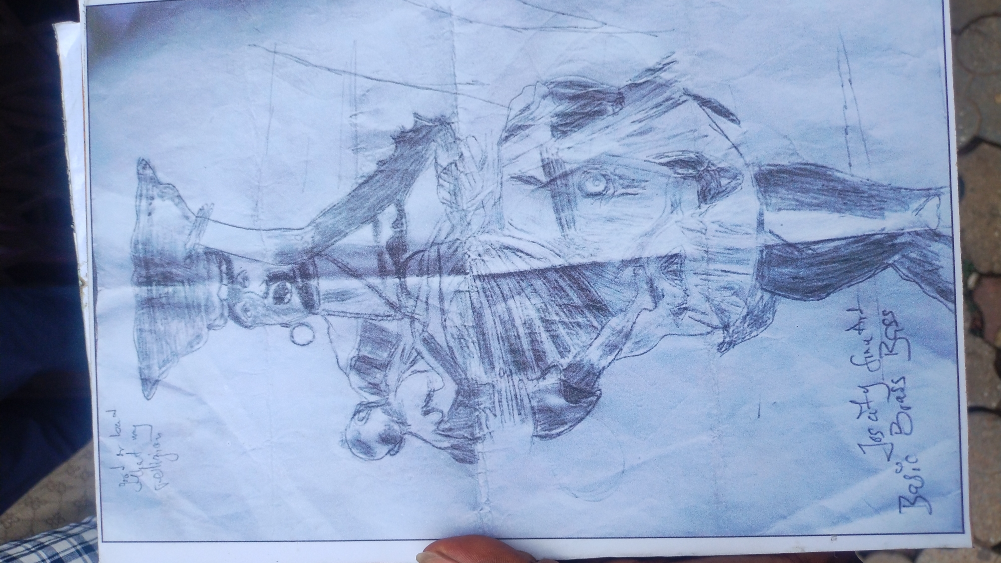 A piece of creased white paper, held by a dark-skinned hand visible on the left, displays a pencil drawing. The drawing depicts a standing female figure with a small child strapped to her back. The central figure has a large, rounded object, possibly a basket or bowl, balanced on her head. Her left arm (viewer's right) is raised, holding an indistinct, thin object, potentially a staff. Her mouth is open. She has a prominent circular earring in her visible left ear. The figure's torso features horizontal lines, resembling ribs or textured clothing, and a visible breast on the viewer's right side. She wears a skirt or wrap around her lower body, and her legs are heavily shaded.
Handwritten text in the top left corner of the paper reads: "good or bad That my religion". In the bottom left, further handwritten text states: "Jos city fine Art" and "Basic Brass Boss".
The paper itself exhibits multiple folds, most notably a horizontal crease running across the midsection of the drawing and several vertical creases.
The background behind the paper is out of focus. The top left reveals a portion of a person wearing a plaid shirt. The bottom shows light-colored paving stones or concrete, indicating an outdoor setting in the city of Jos, Nigeria.