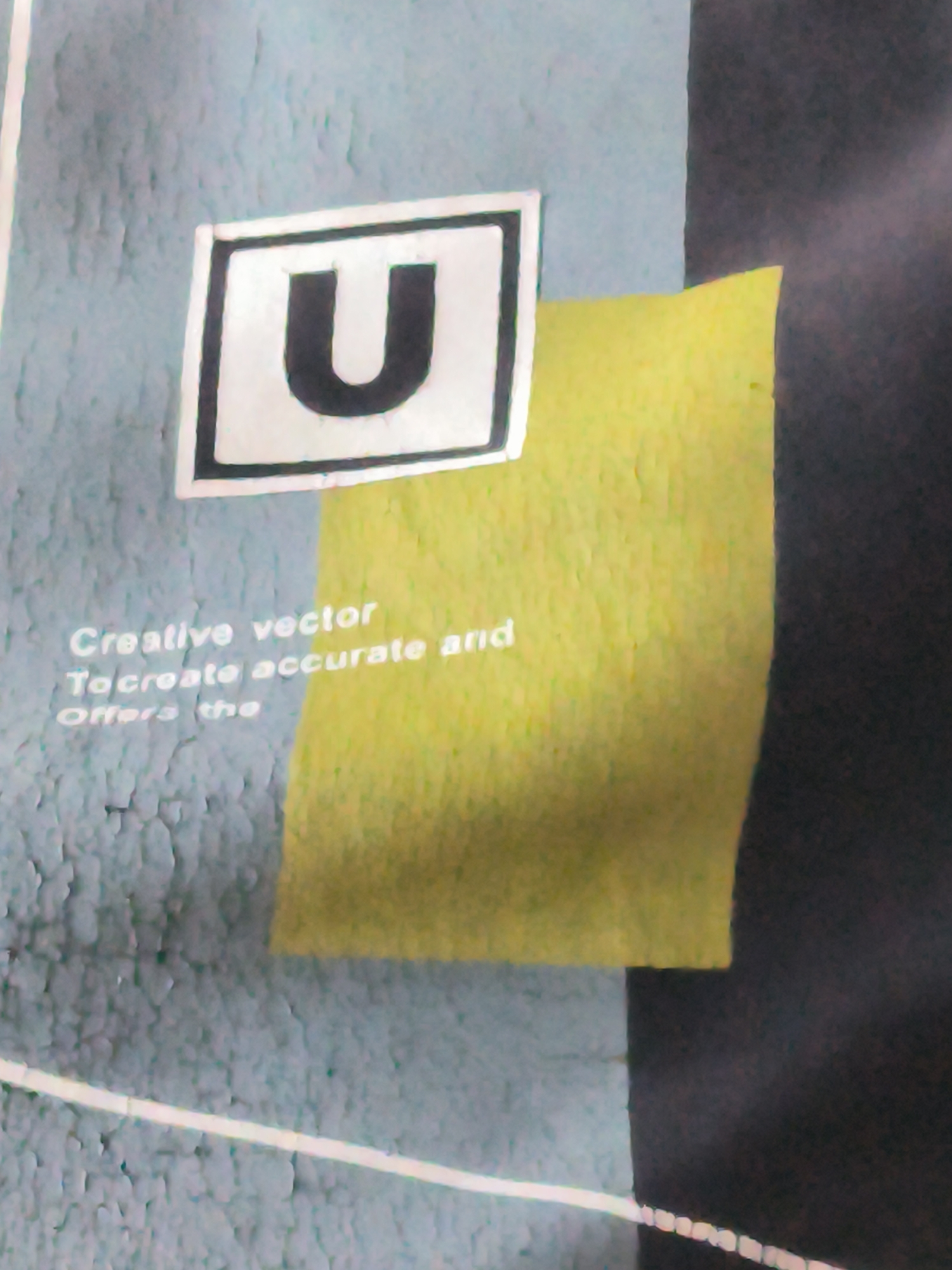 The image is a close-up shot of a design or graphic, not a real-world scene. The design includes a black letter "U" in a white square with a black border. Text reads "Creative vector. To create accurate and offers the". The design has a yellow rectangular element behind the "U" and text. The background includes textures with light blue, yellow and dark grey segments. The image does not depict Lhokseumawe, Indonesia, or any identifiable location.