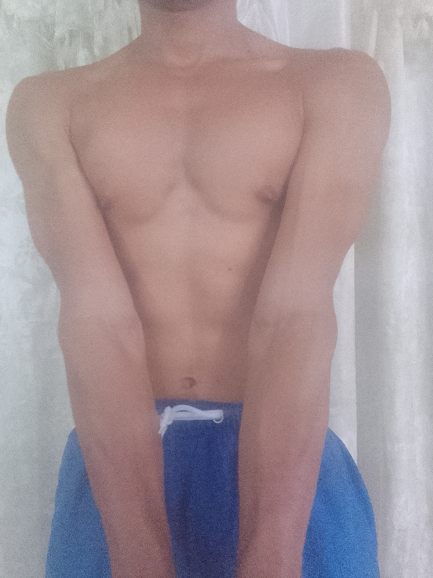 A shirtless person is depicted from the chest down, wearing blue shorts. The person stands in front of a white curtain. The location is not discernible from the provided image.