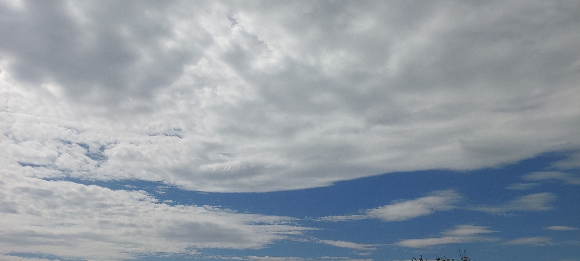 The image depicts a bright, overcast sky with a mixture of white and grey clouds. A strip of clear blue sky is visible towards the bottom of the frame. There are no people, animals, buildings, or identifiable landmarks from Praporştşikovo, Kazakhstan visible in this image. The scene is solely focused on the sky and clouds.