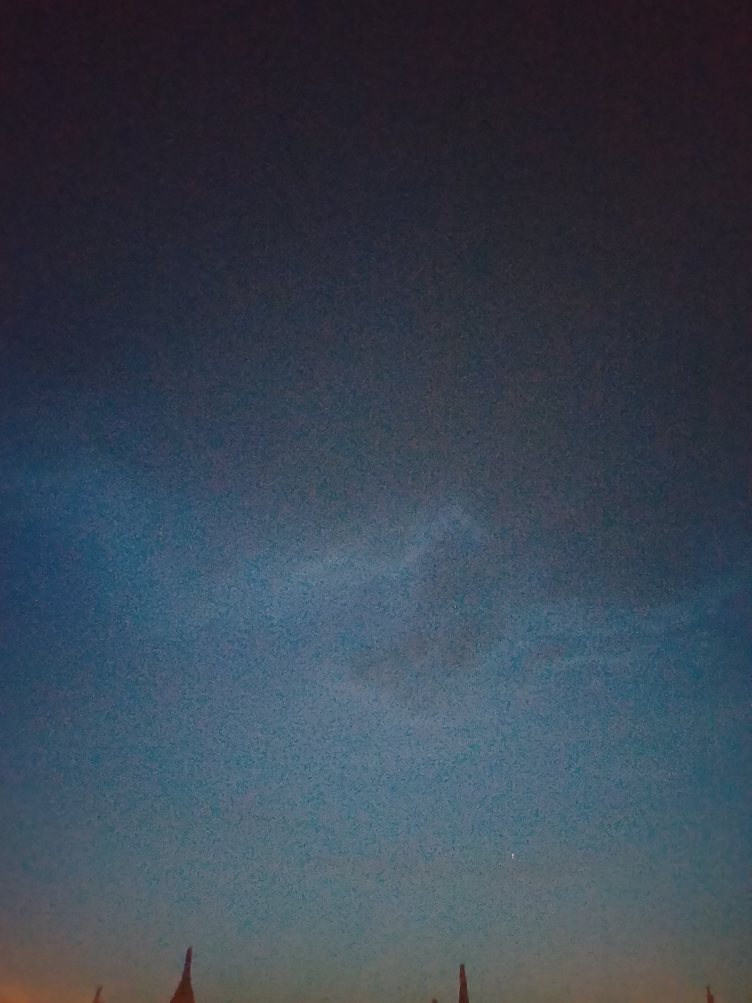 A dark, grainy image shows a night sky fading to orange on the horizon. Silhouettes of structures, potentially buildings, are visible at the bottom of the frame. A single, small light point is visible in the sky. The location, Rido, Nigeria, is based solely on the prompt's request. The image is too unclear to provide specific details about the structures or any potential activity.