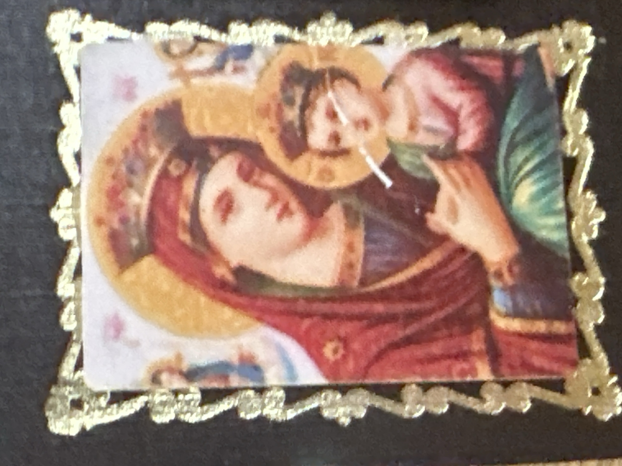 The image displays a religious icon featuring the Virgin Mary and the infant Jesus, framed by an ornate gold border. The Virgin Mary is depicted wearing a red robe and a crown, with a halo. The infant Jesus, also with a halo, is in her arms and appears to be holding a cigarette. The icon is set against a dark background. There is no discernible location information within the image that specifies Marten, Bulgaria.