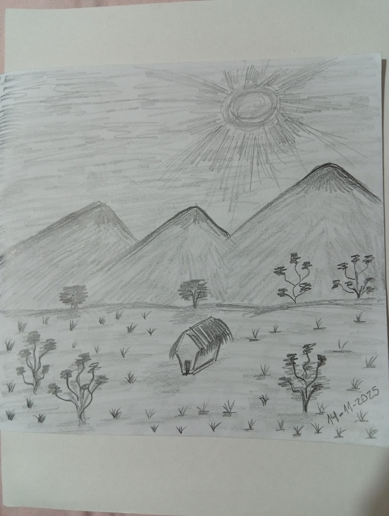 The image is a pencil sketch of a landscape. In the foreground, there are scattered tufts of grass and a few stylized trees with thin branches and small leaf clusters. A small, thatched-roof hut is situated in the middle of the scene. Further back, a series of three mountains dominate the background, with the sun, depicted as a circle with radiating lines, shining brightly in the upper right corner of the sky. The sky itself is filled with horizontal shading lines, suggesting a cloudy or hazy atmosphere. A date, "14-11-2025", is written in the lower right corner. The style of the drawing is simple and somewhat abstract. There are no people or animals depicted in the sketch. This drawing does not depict any identifiable landmarks or features specific to San Antonio de Los Altos, Venezuela; it is a generic landscape scene.