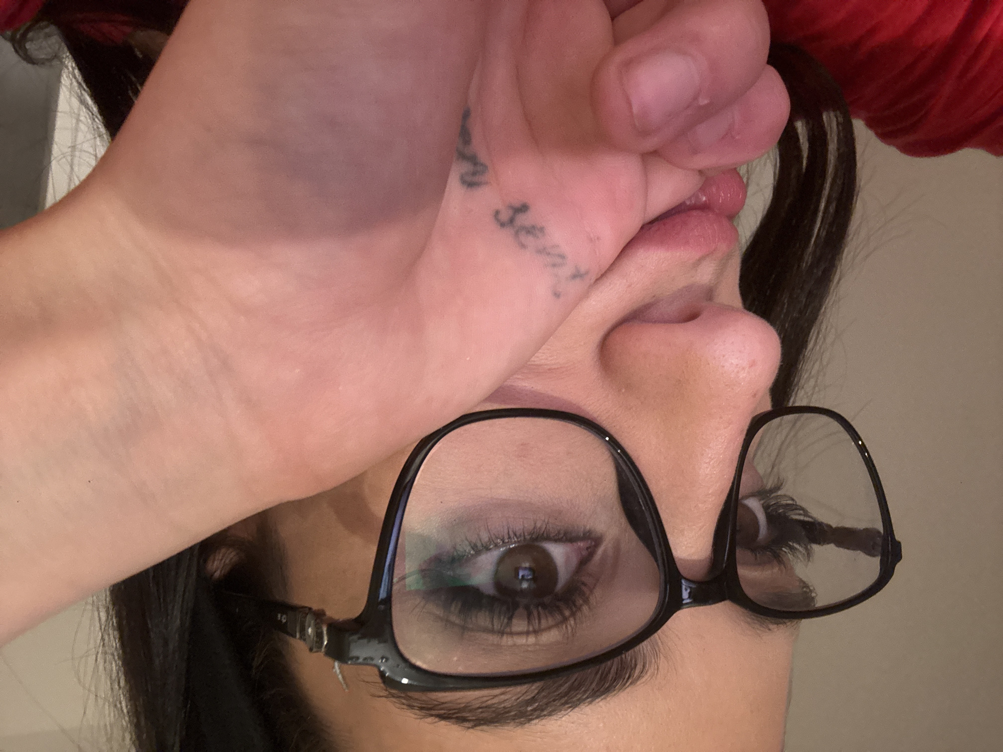 A close-up, slightly blurred image shows a person wearing black-framed glasses. The person's right eye is visible through the lens, along with an eyebrow and some of their nose. Part of a hand covers the upper portion of the face, near the mouth, revealing a tattoo on the palm reading "no sense". Dark hair is visible around the face. The background is a neutral beige color. There is no information in this image to suggest its location is in Buenos Aires, Argentina.