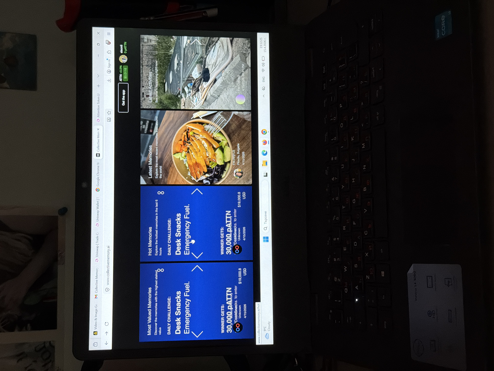 A photograph shows a laptop screen displaying the Collective Memory website. The screen features trending posts and challenges related to the Desk Snacks Emergency Fuel challenge.
One memory is tagged "FM-RRJYJ3, Plovdiv, Bulgaria, 4/15/2026" and shows a bowl with salad and grilled chicken or fish. Another memory is tagged "FM-CMDb2, 4/15/2026, 08:21 PM" and appears to show a damaged building or debris, the source or location of which is not otherwise specified.
The laptop is a black Dell Vostro 14 3000, with a sticker indicating it uses an Intel Core processor. The keyboard has Cyrillic characters. The time displayed on the screen is 23:12:25, and the date is 15.4.2026.