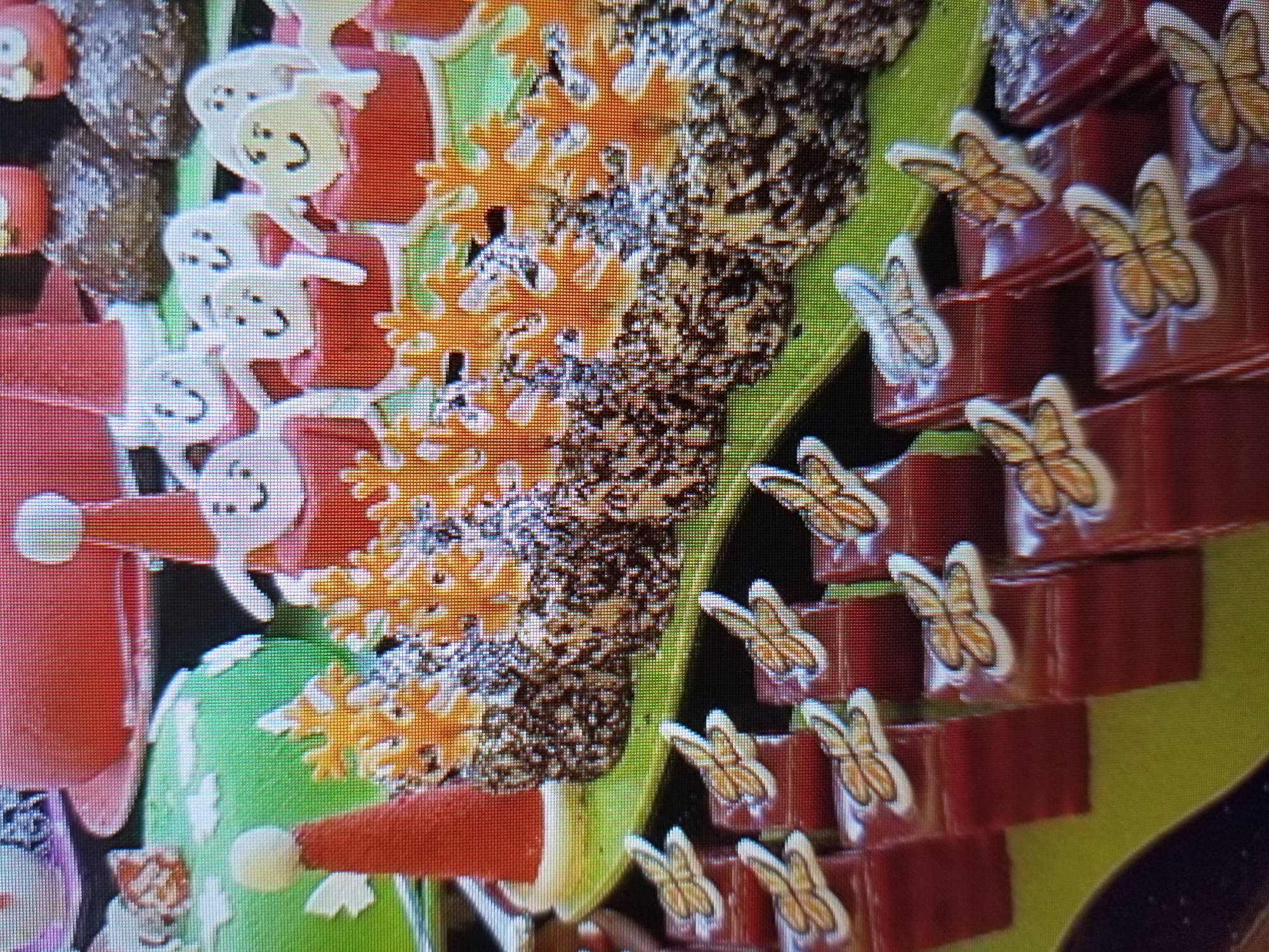 The image shows a display of Christmas-themed desserts. In the foreground, there are rows of small, rectangular red cakes topped with butterfly-shaped decorations. Behind these, there are several small, round cakes covered in chocolate sprinkles and topped with smiling white gingerbread figures wearing Santa hats. Further back, there is a large green cake decorated with white frosting and red candy elements, as well as a large red cake. The desserts are arranged on a green surface. The image does not contain information about the city of Tiraspol, Moldova.