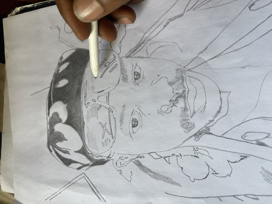 A dark-skinned hand holds a white blending stump, actively working on a pencil drawing rendered on white paper in an indoor setting in Jos, Nigeria. The drawing depicts a male subject from the shoulders up, wearing a dark head covering with lighter patterns. Sunglasses are pushed onto his forehead, exhibiting distinct "X" and "A" shaped reflections or designs on their lenses. The subject also features a mustache and a chin beard. The blending stump is positioned over the right lens of the drawn sunglasses, indicating an ongoing blending or shading action. The white paper shows minor creasing along its top edge, and the artwork remains partially unfinished, with areas of shading complementing initial outlines.
