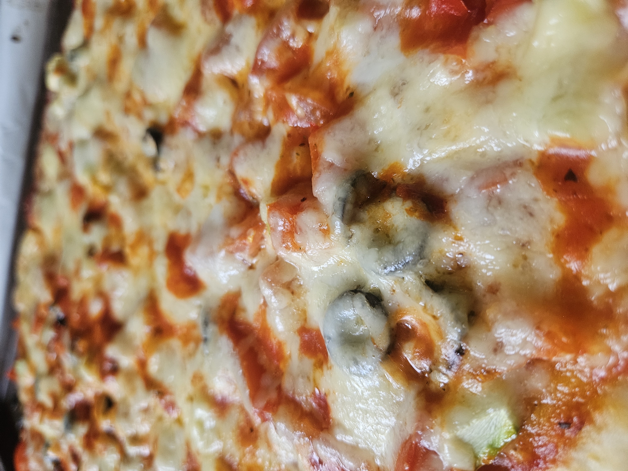 The image shows a close-up of a pizza with melted cheese, tomatoes, and what appears to be olives or mushrooms. The pizza is likely rectangular. It is impossible to confirm that this photo was taken in Rodniki, Russia based on visual information alone.