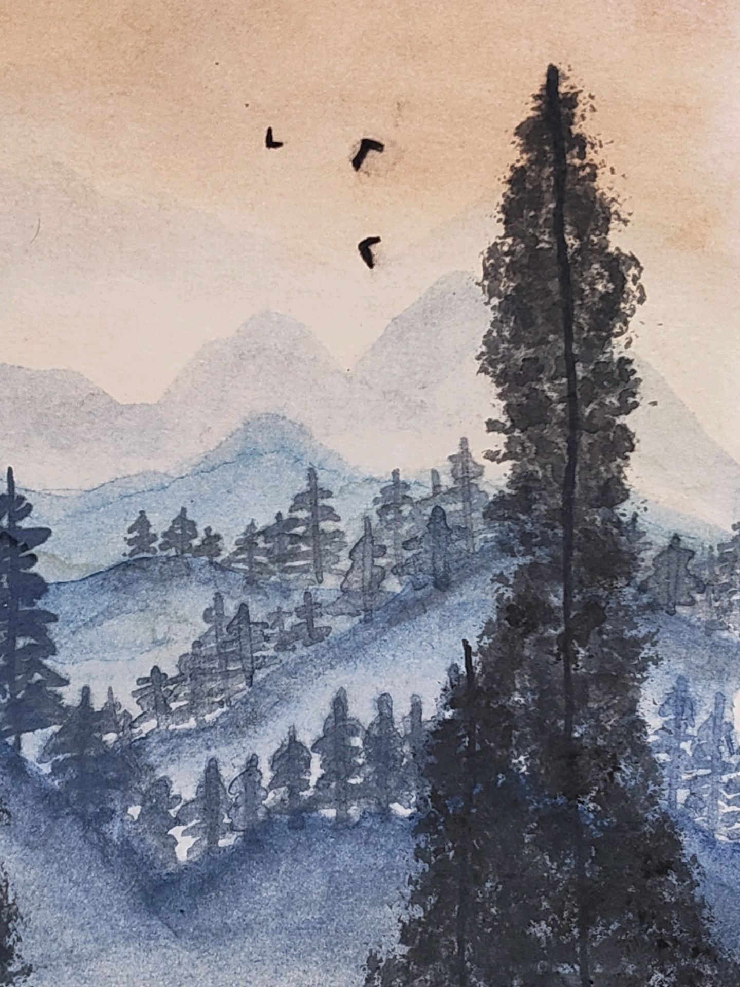 This is a watercolor painting of a mountainous landscape. In the foreground, a tall, dark evergreen tree dominates the right side of the frame. Behind it, rolling hills are depicted with layered washes of blue watercolor, dotted with smaller evergreen trees. Further in the background, several mountain ranges are rendered in lighter shades of blue and gray, fading into a soft, peachy-orange sky. Three small, dark shapes, possibly birds, are visible in the upper left portion of the sky. The painting style is impressionistic, with visible brushstrokes and blended colors. This painting is not located in Mysuru, India, as the scene depicts a mountainous, forested environment.