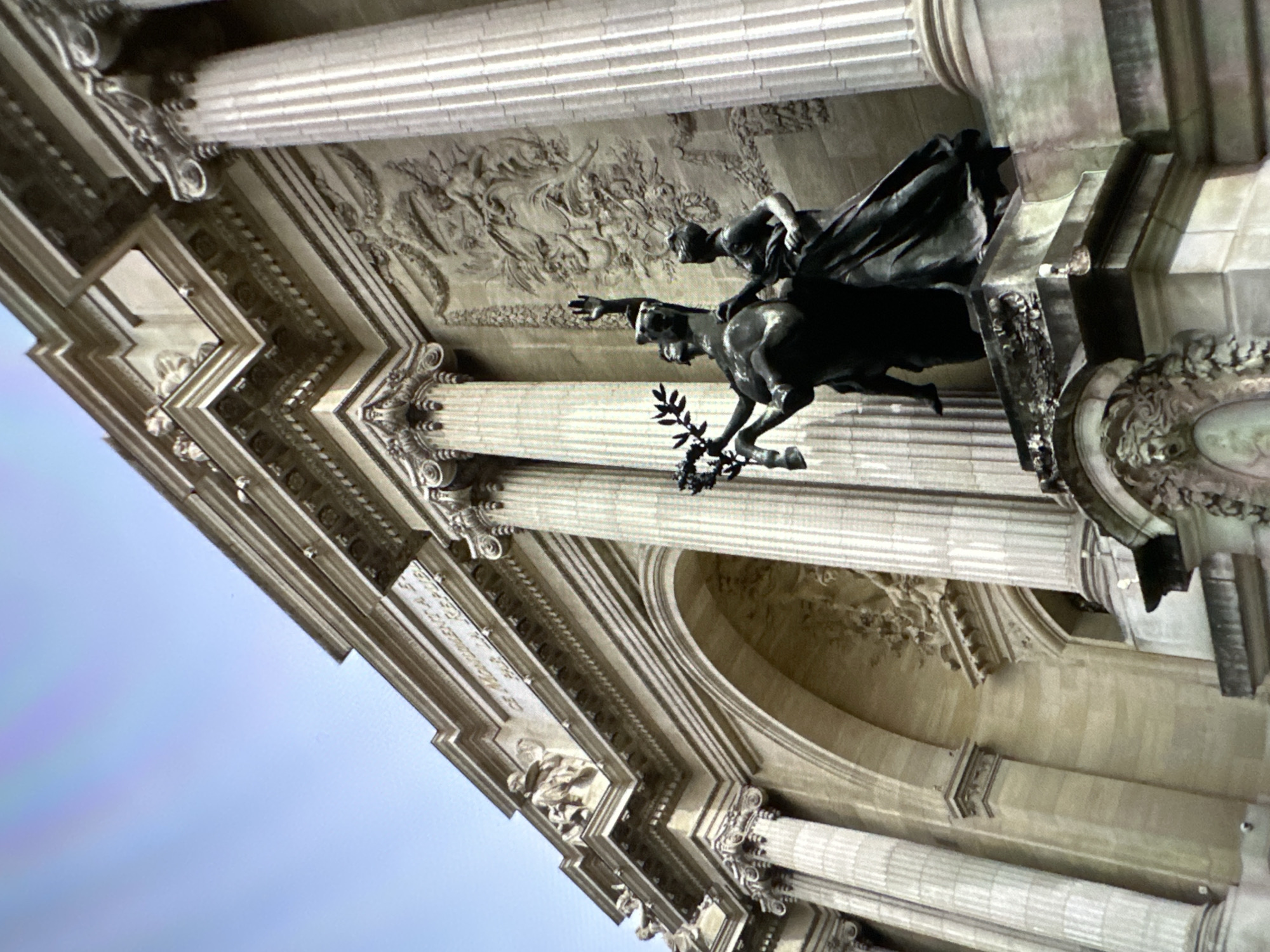 The image captures a low-angle view of an architectural facade adorned with classical features. Fluted columns support an entablature with intricate carvings and moldings. A bronze sculpture of a horse and rider is mounted above the columns, the rider reaching forward, while the horse holds a laurel wreath.
While the image features neoclassical architecture, I cannot confirm whether it is located in Chișinău, Moldova. Further information about the location would be required for complete accuracy.