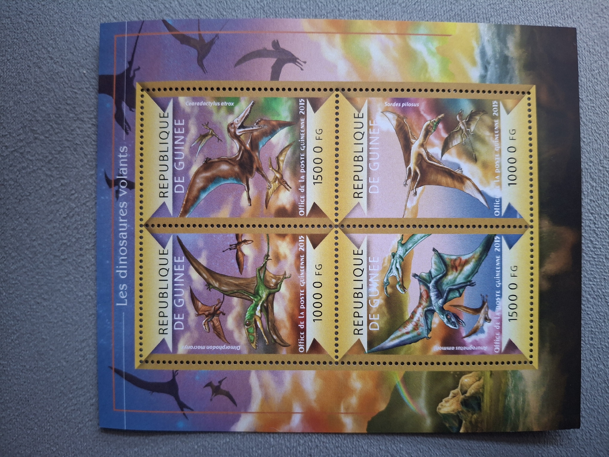 The image shows a sheet of postage stamps from the Republic of Guinea. The stamps are arranged in a 2x2 grid within a larger illustrated frame. Each stamp depicts a different flying dinosaur. The stamps include the name of the dinosaur (Cearadactylus atrox, Sordes pilosus, Dimorphodon macronyx, Aurognathus ammoni), the country name "Republique de Guinee", the value (1000 or 1500 FG), and the text "Office de la Poste Guineenne 2015". The outer frame is printed with images of flying dinosaurs. The title "Les dinosaures volants" is printed on the left side of the frame. The image provides no information about Pleven, Bulgaria.