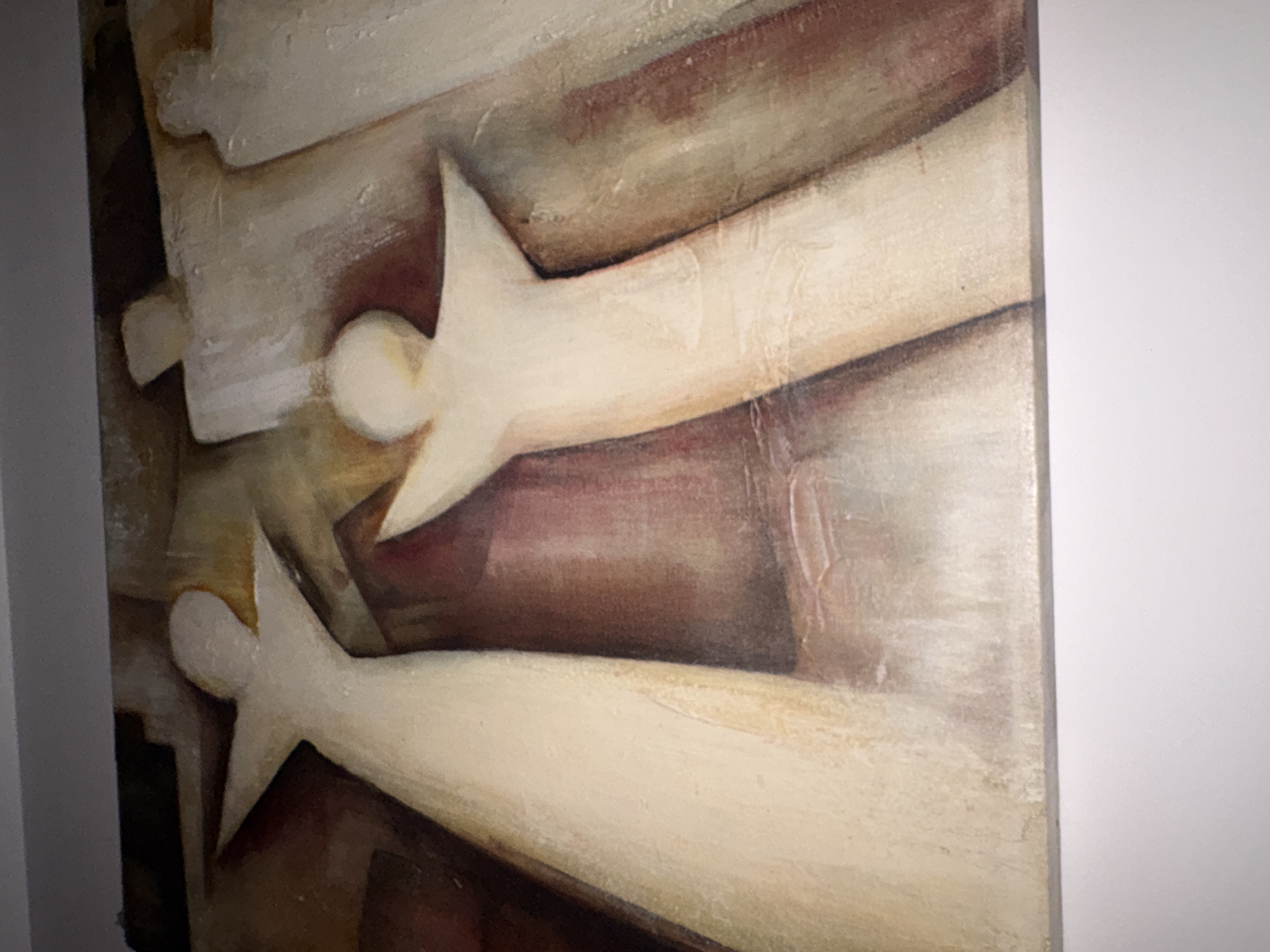 The image captures a close-up view of a semi-abstract painting, likely executed in oil or acrylic on canvas. The artwork predominantly features two highly stylized figures, rendered in a light, creamy white hue. These figures are characterized by simplified, spherical heads and elongated, tapering bodies that include prominent, sharp, wing-like or arm-like extensions. They are positioned diagonally across the canvas, creating a sense of upward movement or dynamic ascension.
The background of the painting presents a textured blend of warm, earthy tones, including deep browns, muted reds, and hints of ochre or dark yellow, providing a strong contrast to the luminous figures. Visible brushstrokes and areas of impasto contribute to the tactile quality and depth of the artwork. The figures evoke an ethereal or spiritual presence, resembling angels or ascending spirits. There is no discernible activity beyond their suggested movement or state of being. No text is visible on the painting. This artwork is located in Mexico City, Mexico.