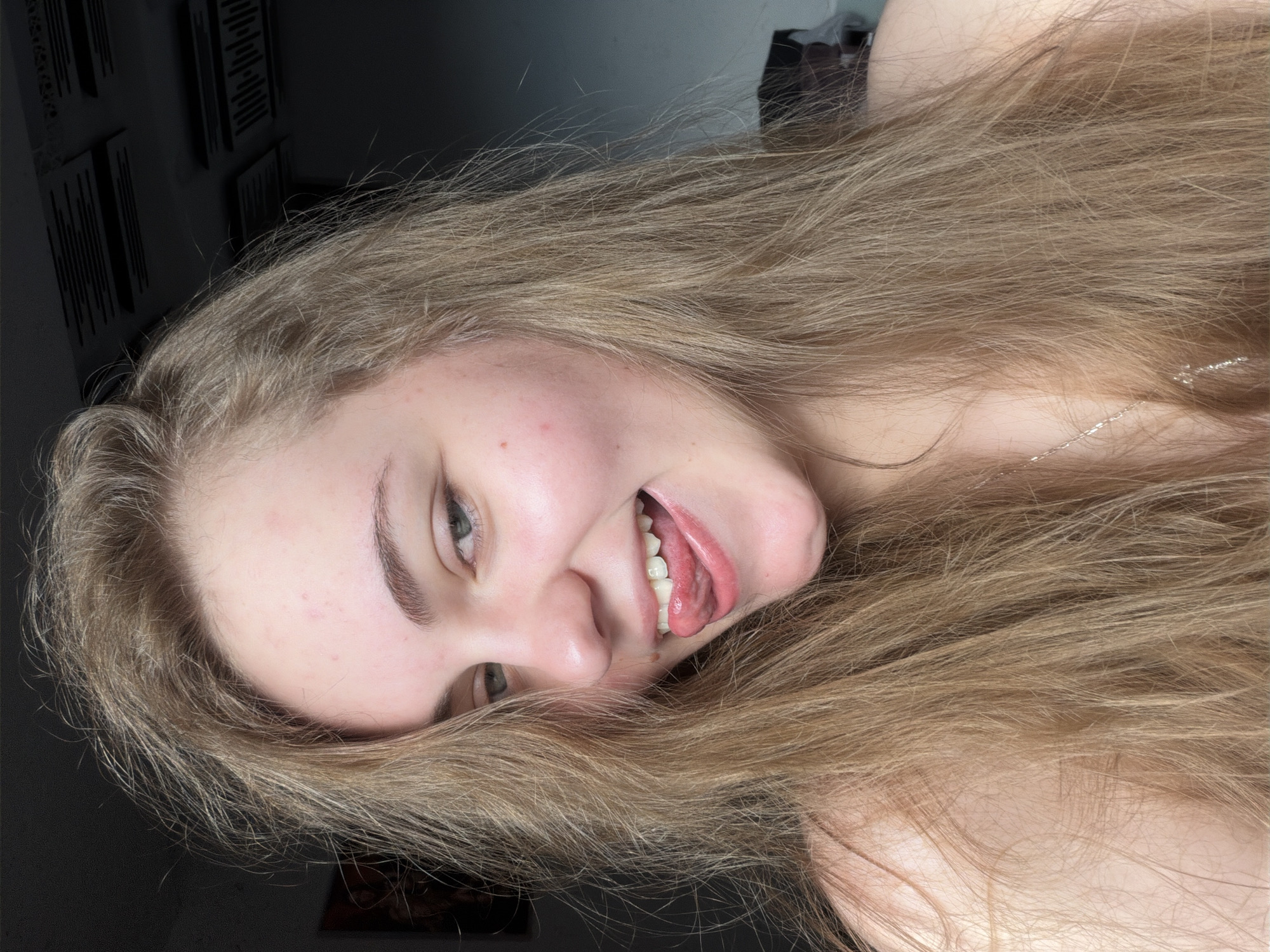 A young woman with long, blonde hair is shown in a close-up selfie. Her head is slightly tilted, and her tongue is sticking out. Her eyes are open, and she is smiling. The background is dark, with what appears to be acoustic foam panels visible on the ceiling. The image does not provide any information about the location in the city of Dnipro, Ukraine.