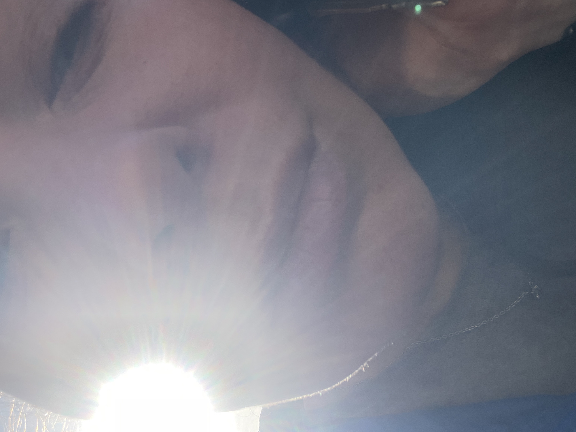 The image shows a person's face partially obscured by bright sunlight, likely taken from a low angle. Facial features visible include an eye, nose, and mouth. The person wears a chain around their neck. The location, Chaikovsky, Russia, cannot be determined from the image content.