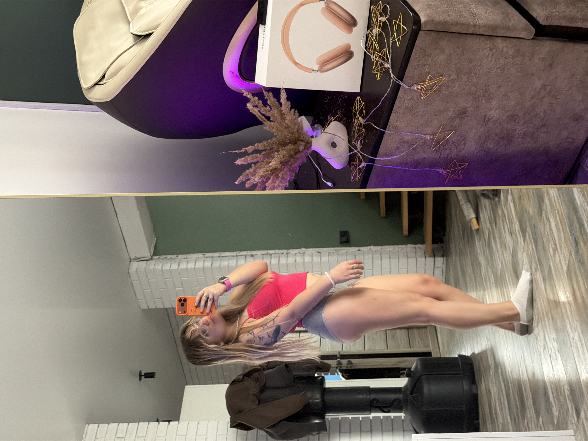 The image shows a split view of two separate scenes. The top half displays a room interior with a hanging egg chair, a side table with a vase of dried flowers, headphones in a box, and string lights. The bottom half shows a woman taking a mirror selfie in what appears to be a home gym. She is wearing a pink top and grey shorts. A punching bag is visible in the foreground. Location: Большая Шильна, Russia is assumed.