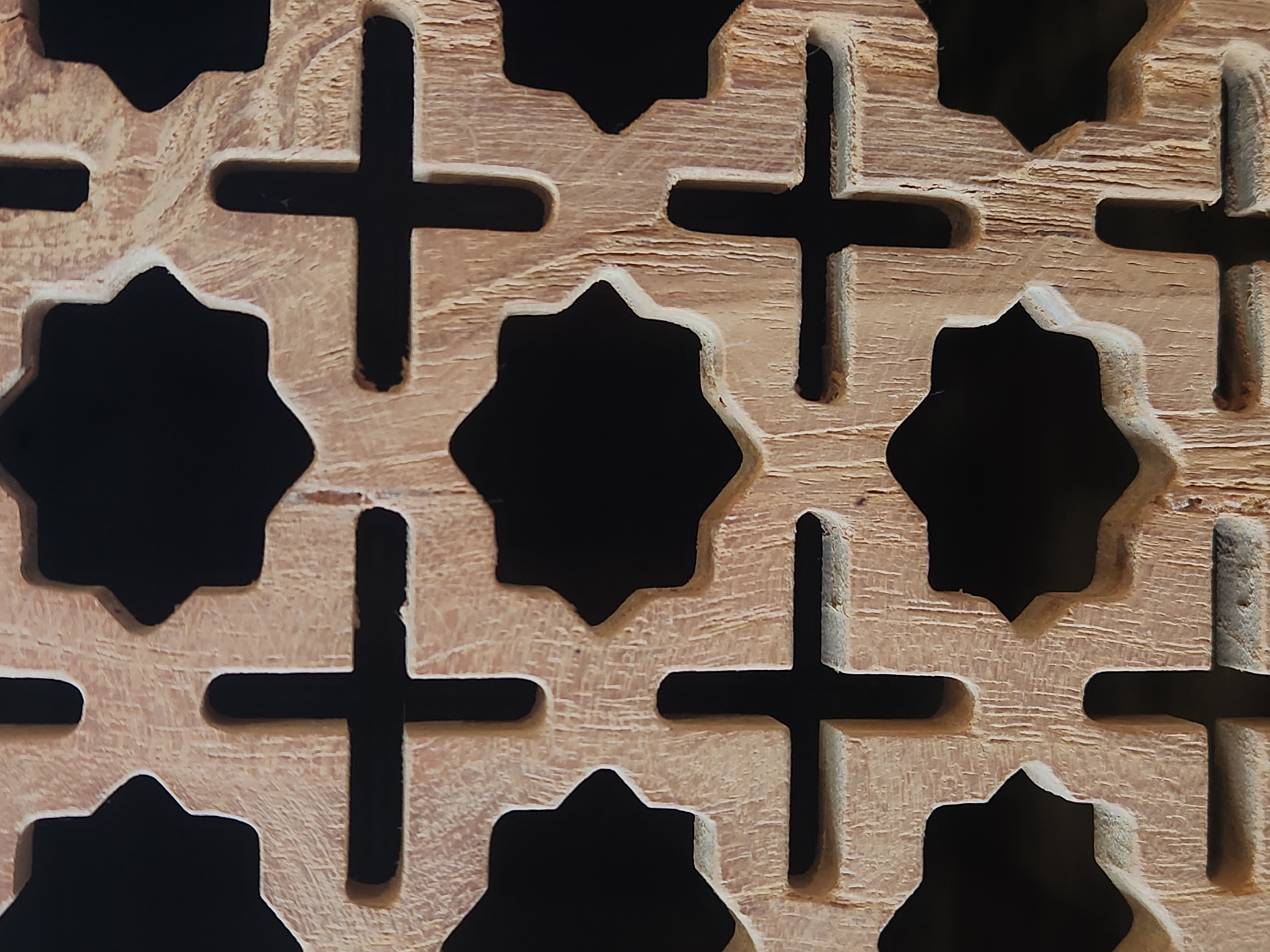 The image displays a close-up, vertical shot of a wooden lattice with a repeating pattern of crosses and octagonal shapes. The wood has a light brown, weathered appearance with visible grain and some imperfections. The background is entirely black, creating a stark contrast that emphasizes the intricate details of the carving. The lattice appears to be an architectural element, possibly part of a screen, window, or decorative panel. No people or discernible environment are visible, suggesting the focus is solely on the texture and design of the object itself. The location is specified as Maitland, United States of America, however, the image does not provide any visual cues to confirm this location.
