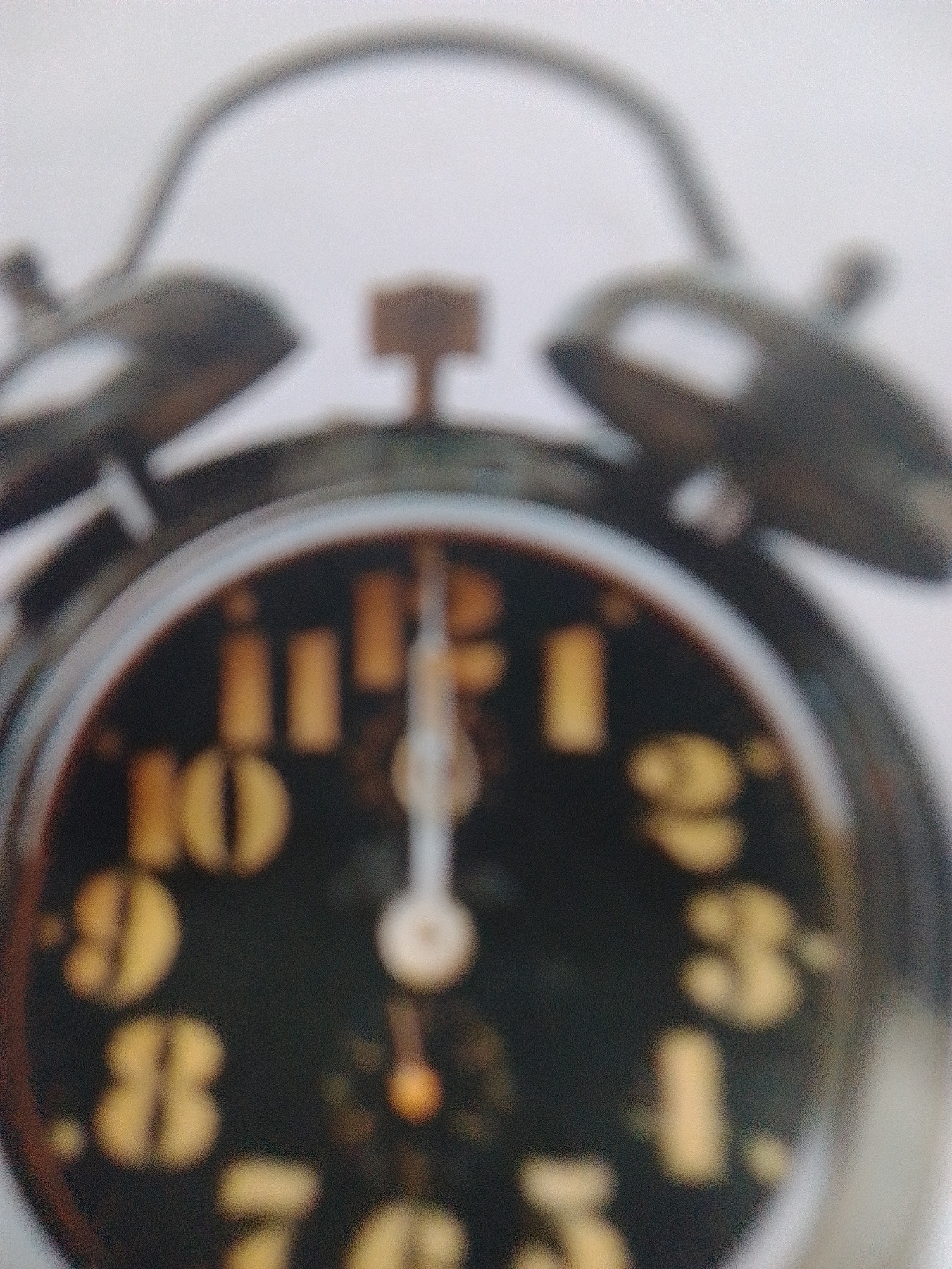 This media file shows a close-up, out-of-focus image of an analog alarm clock. The clock has a dark face with yellow numerals and hands. The alarm bell mechanism is visible at the top, along with the winding knobs. The hands of the clock are pointing to approximately 12:00. The overall impression is that of an old or vintage alarm clock, possibly a desk clock. There are no people or significant environmental details visible. The image is grainy and lacks sharp focus, making precise identification of all elements difficult. There is no visible text within the image. The context of La Tagua, Venezuela, suggests this is a domestic or personal item.