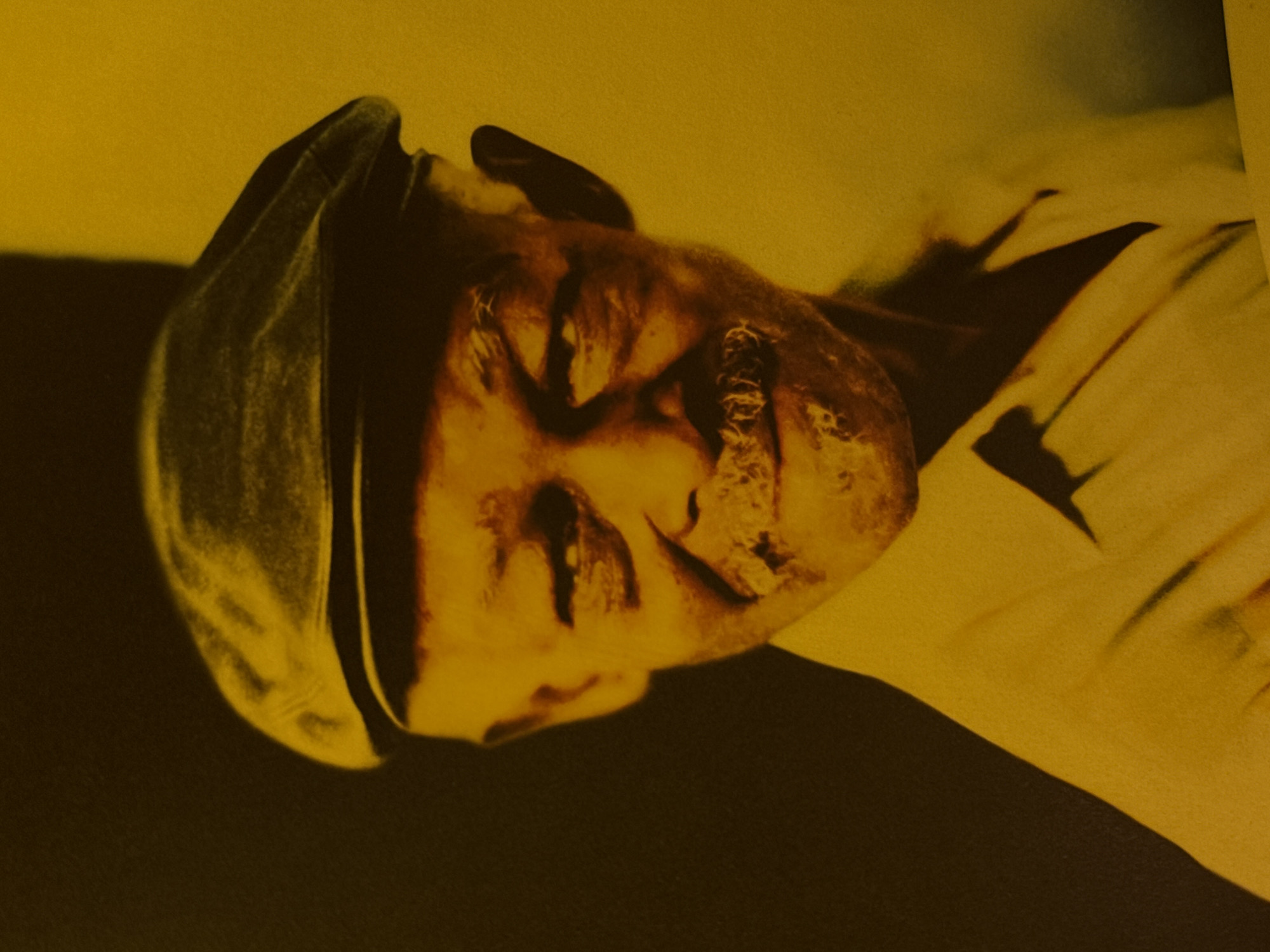 The image appears to be a photograph of the mummified body of King Menkaure, also known as Mycerinus. Menkaure was an ancient Egyptian pharaoh of the Fourth Dynasty during the Old Kingdom. The head is covered with a hat, and the body is laying down. It is in a yellow lighting, which makes the mummy looks gold. The location is likely the Erebuni Museum in Yerevan, Armenia, which houses a collection of artifacts from ancient civilizations.