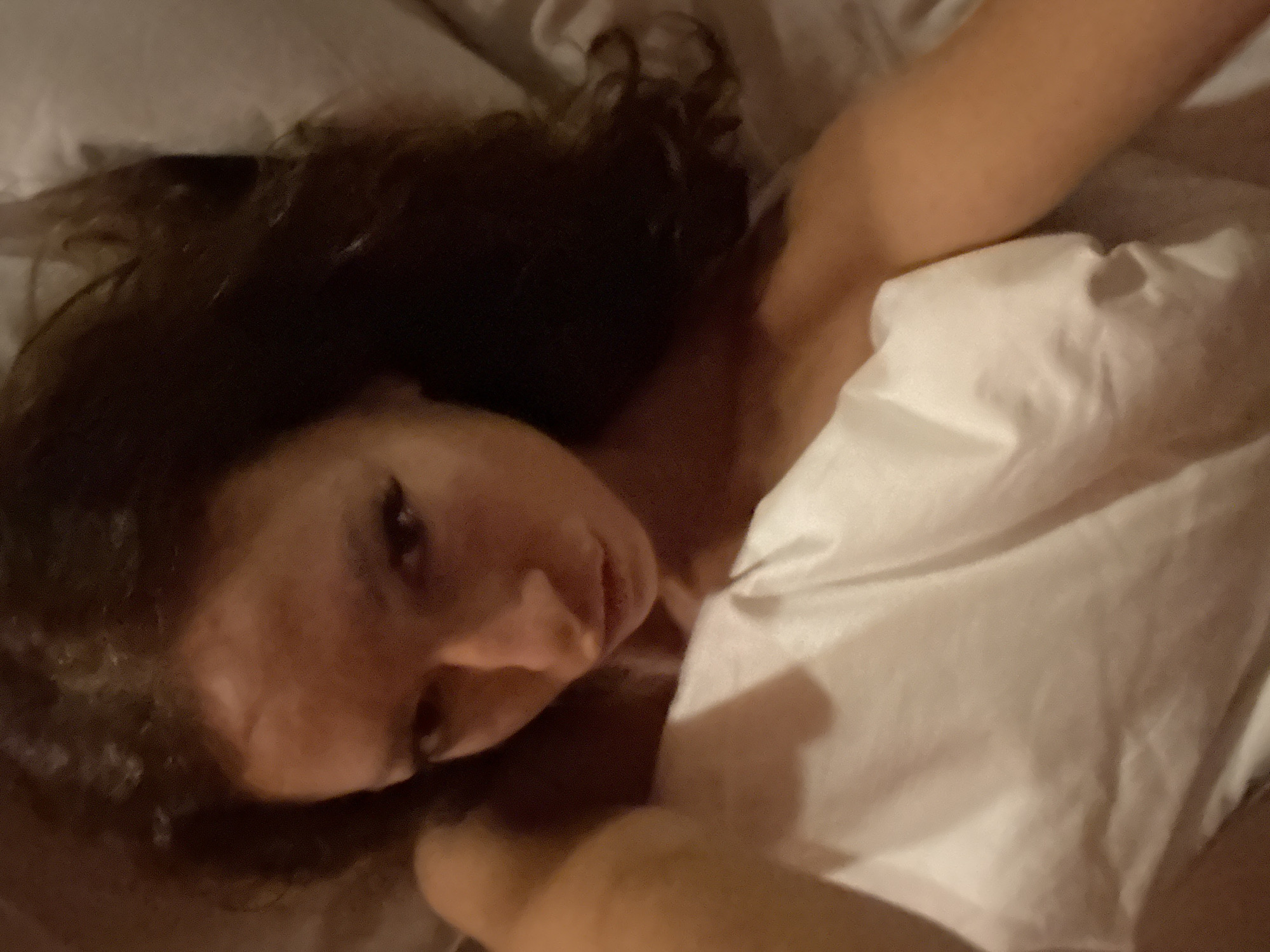 A person with dark, curly hair is lying on white bedsheets. The person's head is turned towards the viewer. The upper body is partially covered by the bedsheets. One arm is visible above the sheets.
This image was not taken in the city of Binh Lu, Vietnam and there is no indication of location to be able to identify it.