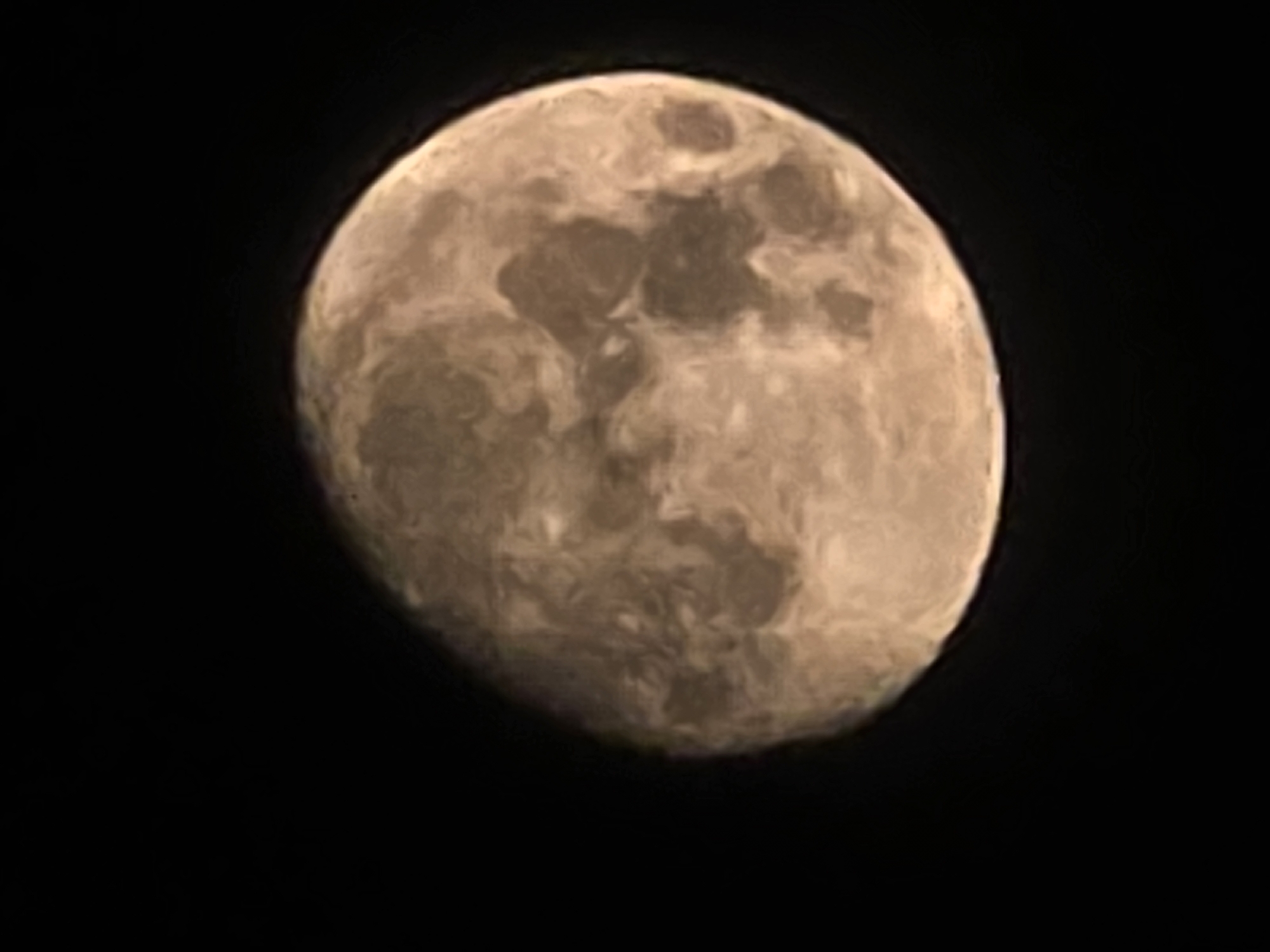 A full moon is visible in the night sky, casting a warm, yellowish-orange glow. Its surface is textured with craters and maria, creating a pattern of light and shadow across its visible face. The moon is positioned to the right of the frame, against a deep black background of the night sky.