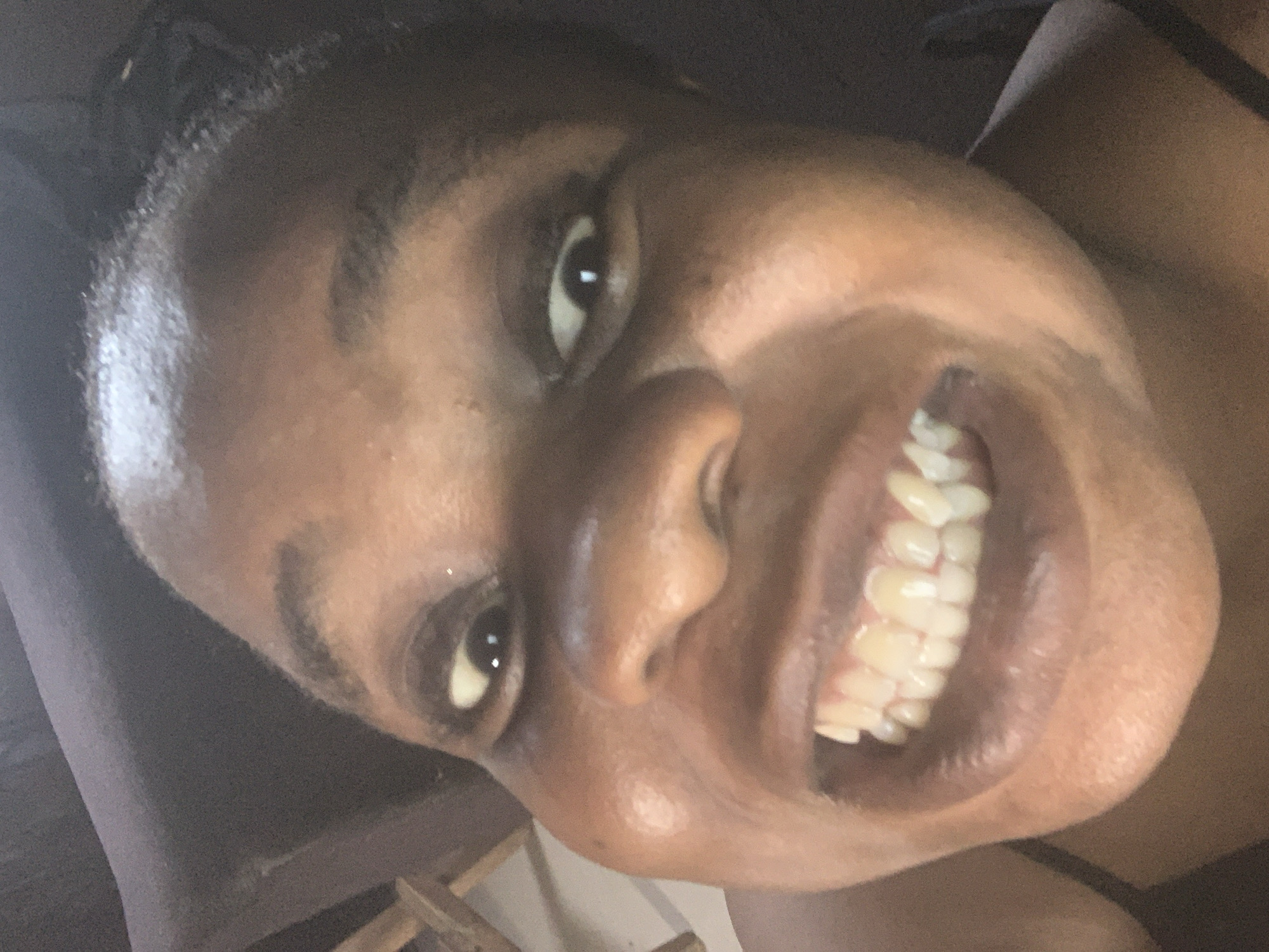 A close-up shot captures a woman's face, tilted towards the camera. She has dark skin, dark eyes, and a wide smile exposing her teeth. The background is blurry and undefined. The location in the city of Unknown, Unknown cannot be determined.