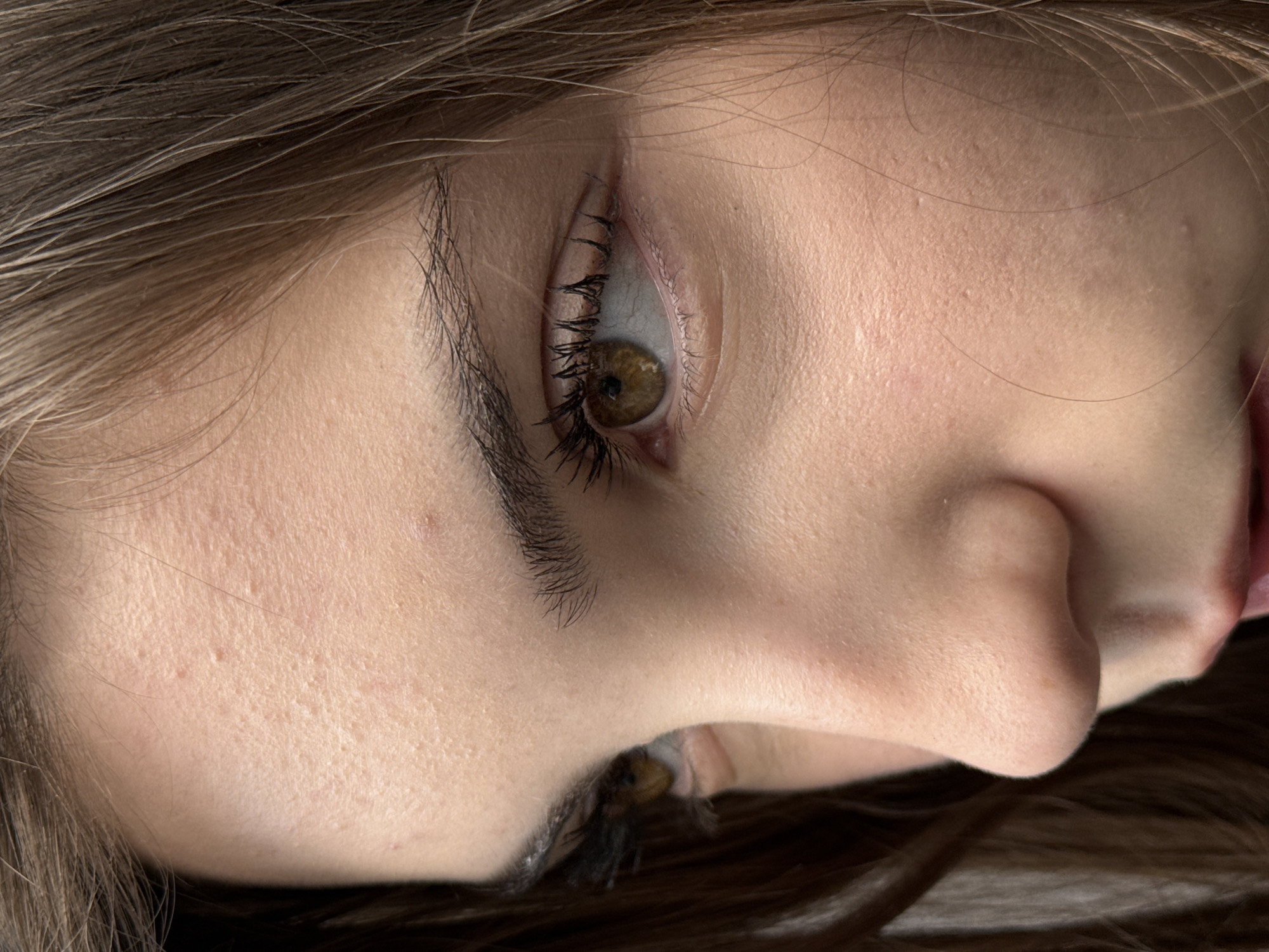 A close-up image shows a person's face in a sideways orientation. The left eye is prominently visible, with brown iris and black eyelashes and eyebrow. The skin appears fair and shows some texture and minor blemishes. The nose is visible, and a glimpse of the mouth is seen on the right side of the image. The hair is light brown, and strands are visible around the face. The location is not discernible from the image, so the city of Sofia, Bulgaria, cannot be verified.