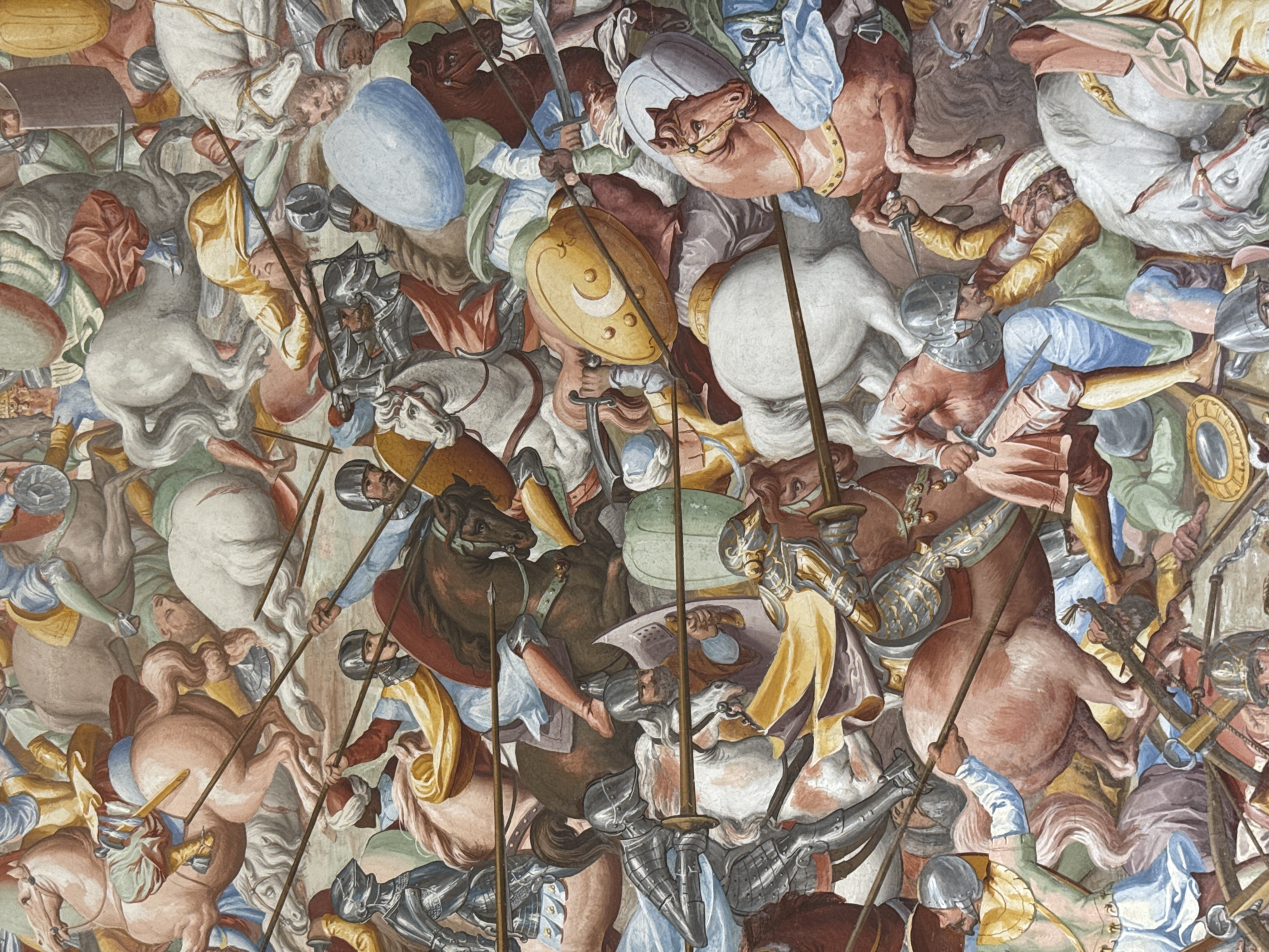 This is a section of a fresco painting depicting a chaotic battle scene on horseback. Numerous figures, both human and equine, are tightly packed together, suggesting a fierce and overwhelming conflict. The people are depicted in a variety of armor and clothing, some wearing elaborate metal suits and helmets, while others are clad in tunics and head coverings. They are engaged in combat, wielding swords, daggers, and lances. Horses are also shown in various states of distress and action, with some appearing to fall or be wounded.
The scene is rendered in rich, vibrant colors, with prominent use of reds, browns, golds, and blues. The details suggest a historical or mythological setting, with an emphasis on the physicality and violence of warfare. There are no overt indications of the time of day or weather, and the setting is abstract, focusing solely on the action. The overall mood is one of intense struggle and disarray, with a sense of urgency and desperation conveyed through the contorted bodies and aggressive postures of the combatants. No visible text is present in the image.