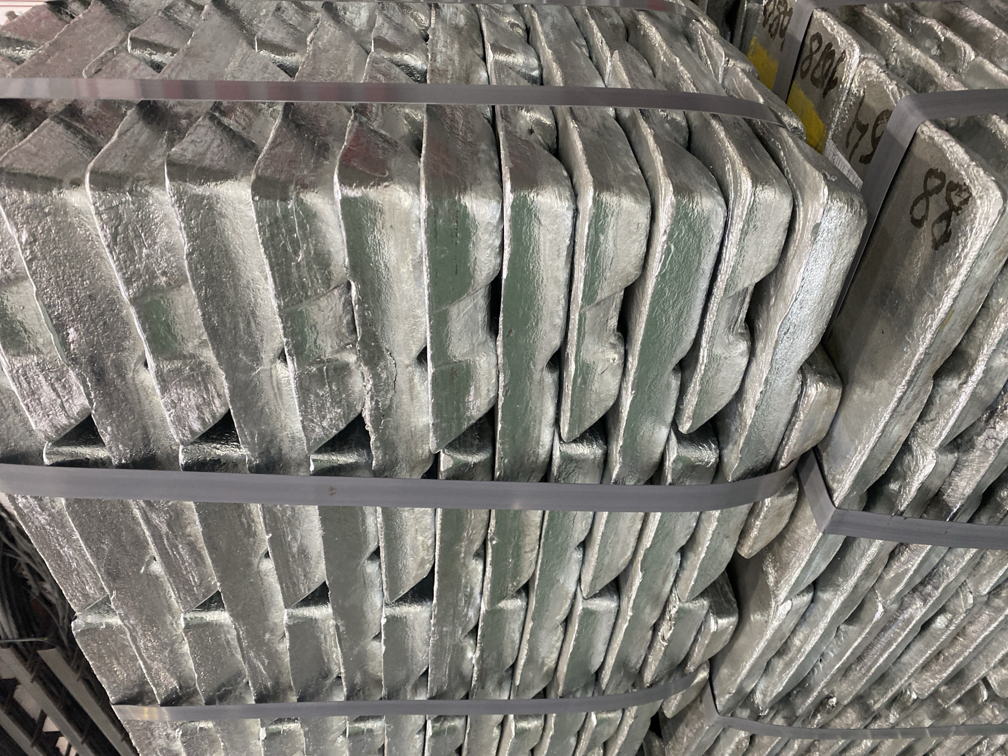 The image shows stacked, silver-colored metal ingots bundled together with gray straps. The ingots are irregularly shaped and have numerical markings on some of them. There is no information to confirm location.
